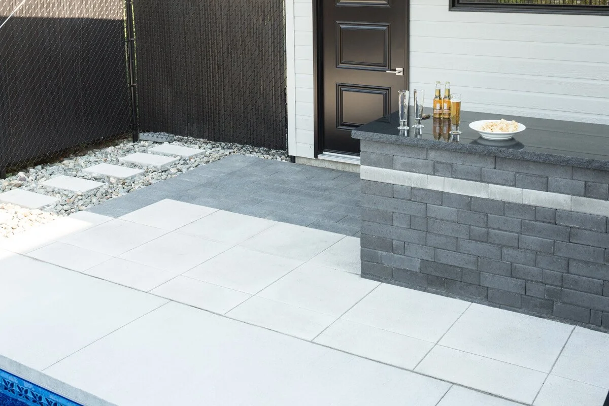 Outdoor patio with gray brick bar, black door, stepping stones on gravel, and bottles with a bowl on the counter.