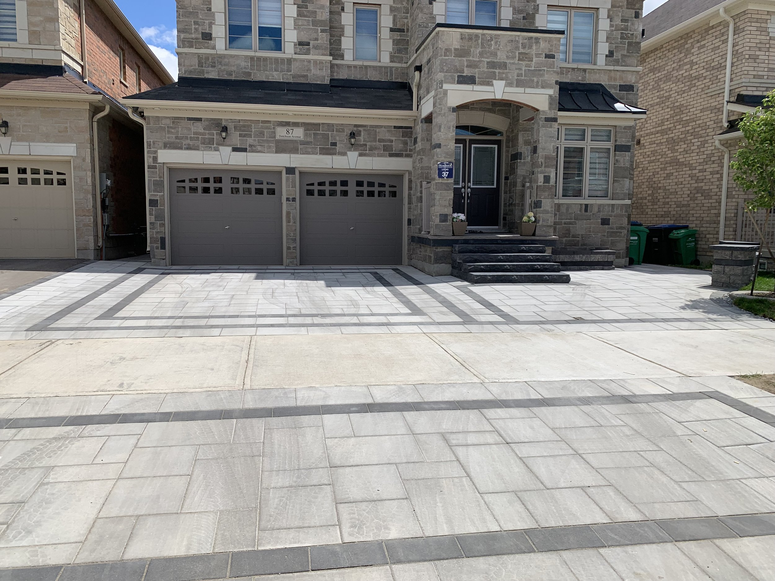 Residential house with a stone exterior, three-car garage, and a newly paved driveway.