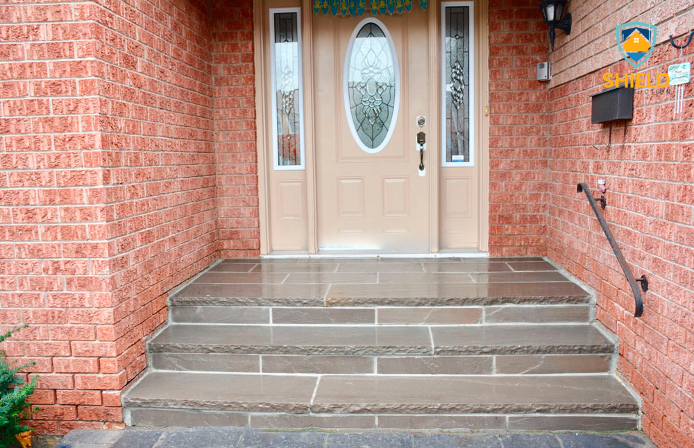 Front entrance of a brick house with a decorative oval glass door, stone steps, and a railing.