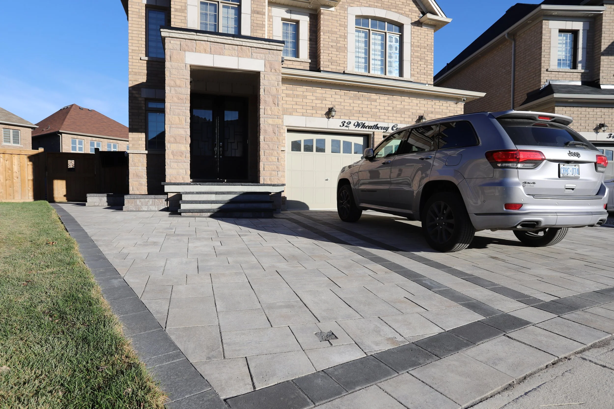 Brick house with a parked silver Jeep SUV on a paved driveway and grass lawn.