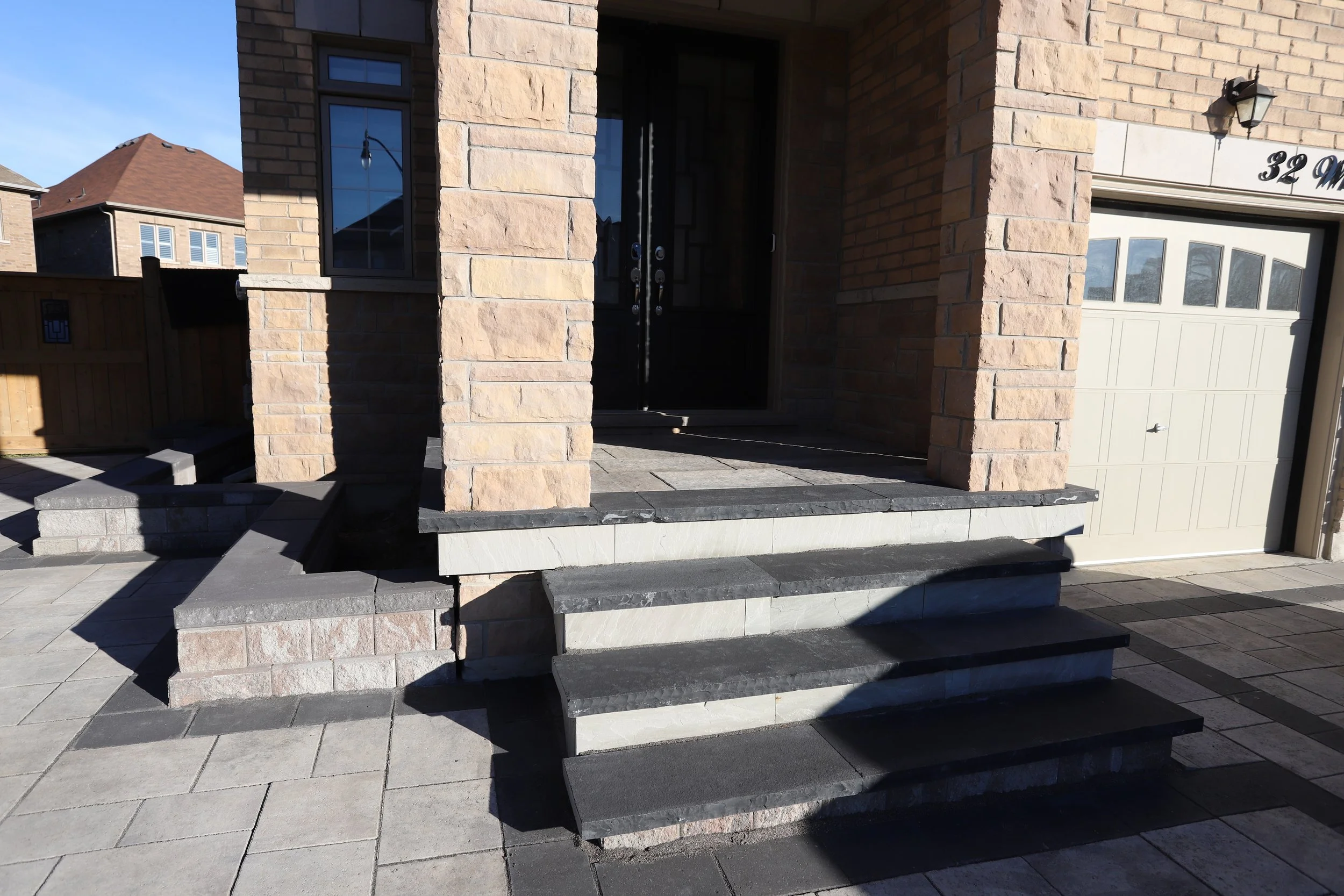 Stone porch of a modern residential home with steps leading to the front door. The house exterior features brick and stonework, and there is a garage visible to the right.