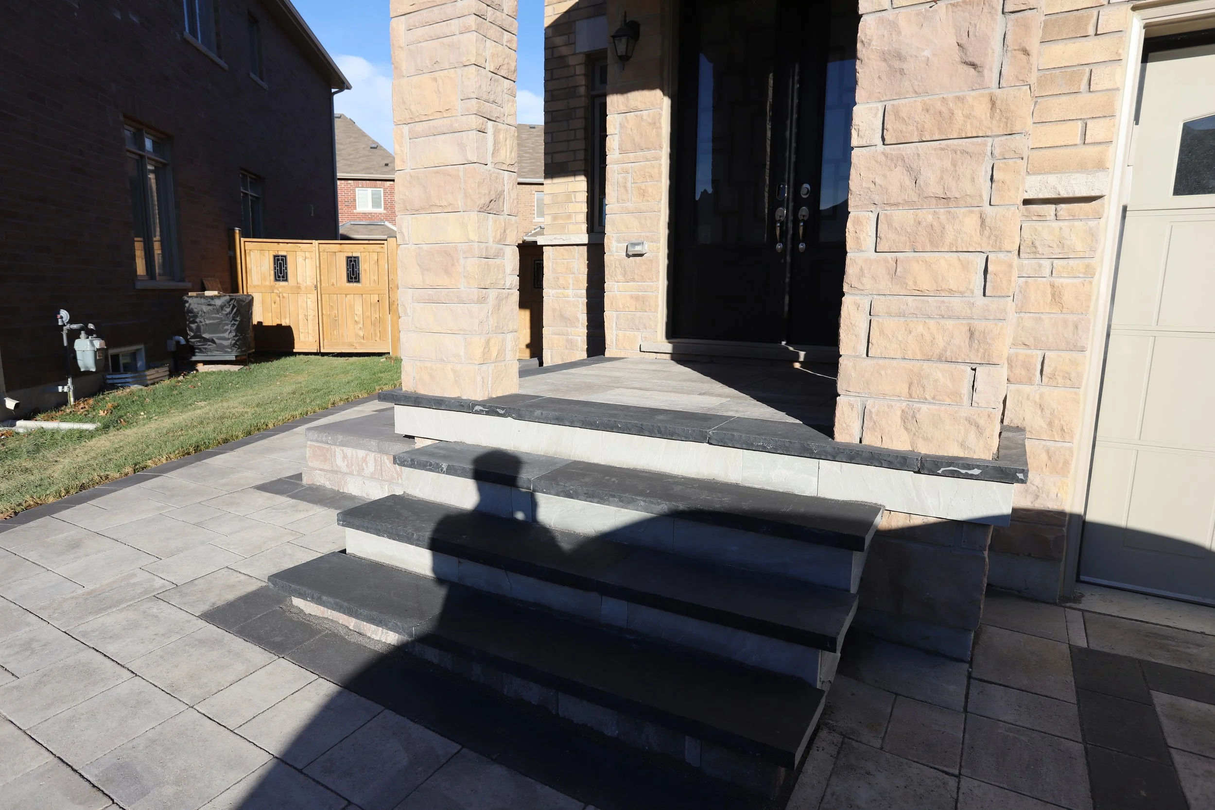 Front porch with steps leading to a stone house entrance, shadow visible on the ground.