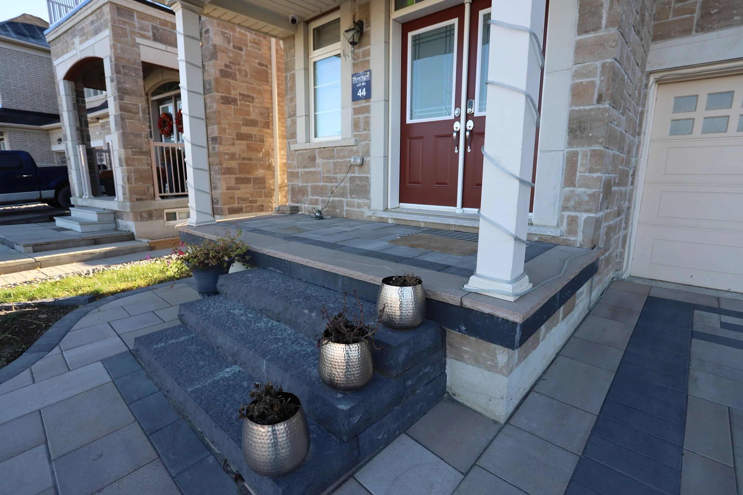 Front porch with stone steps and potted plants in metallic planters, modern brick facade, double doors, and a garage door.