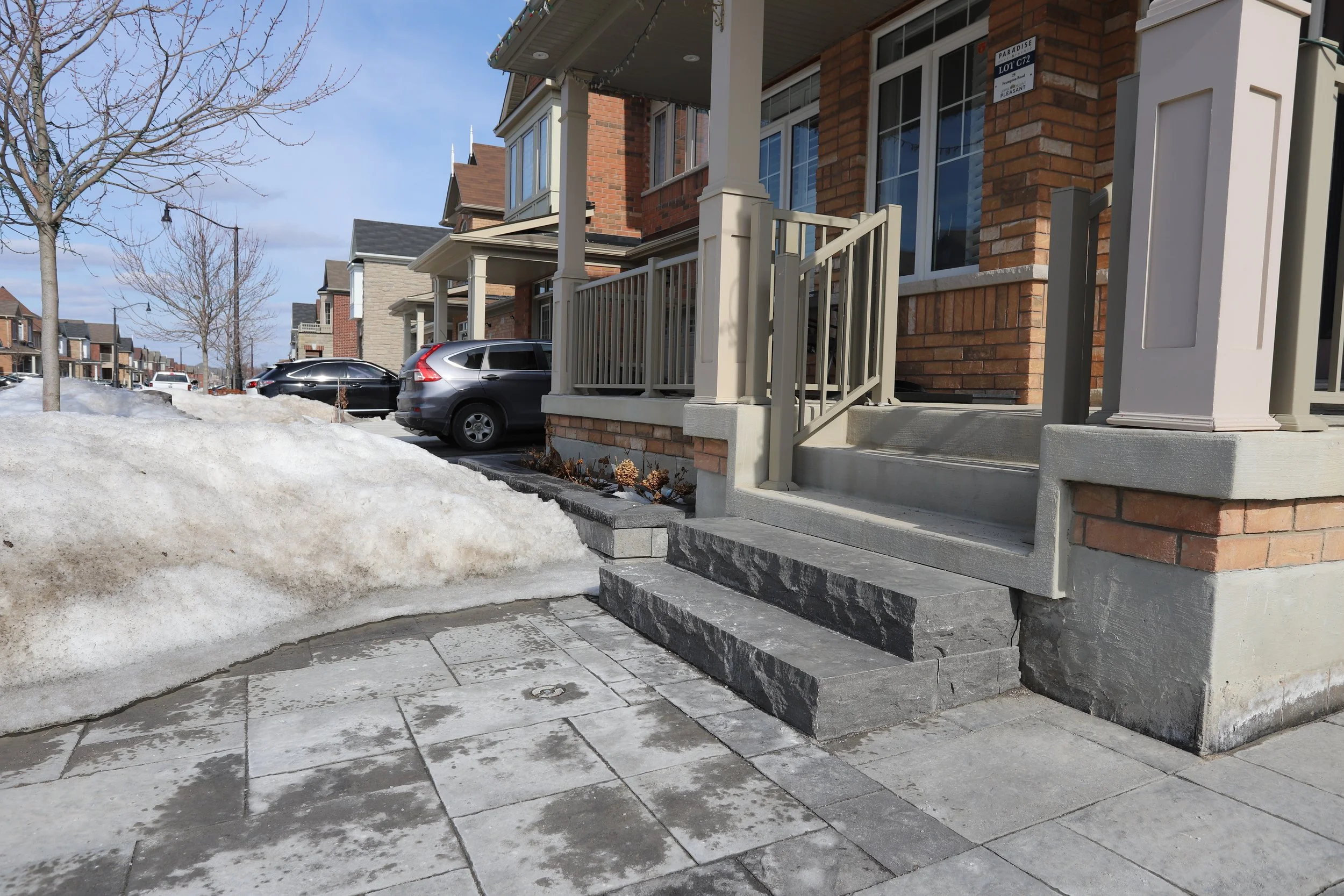 Suburban neighborhood with brick houses, snowy sidewalks, and parked cars.