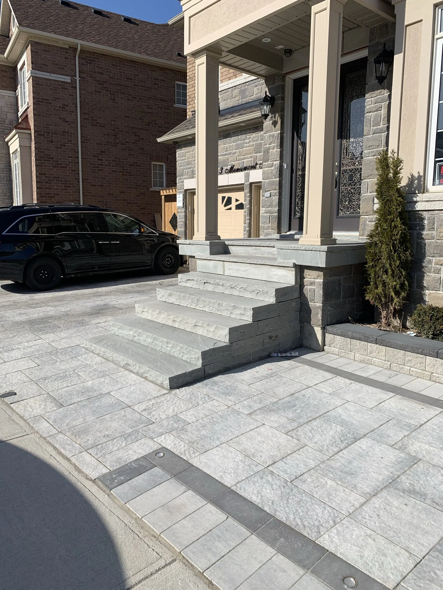Front entrance of a house with stone steps and patio, black SUV parked in driveway.