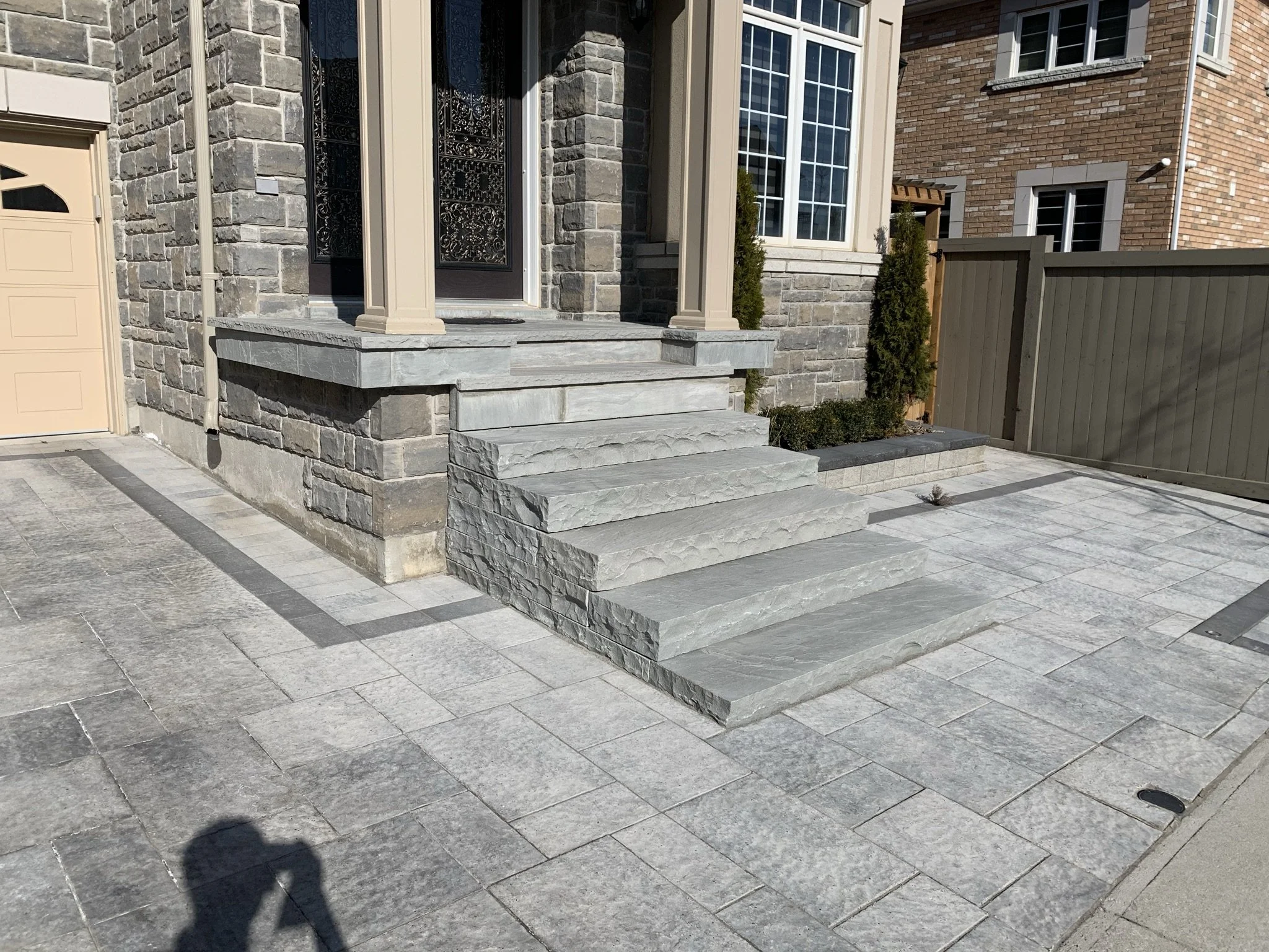 Stone stairs and patio leading to a house entrance with a beige column and stone wall.