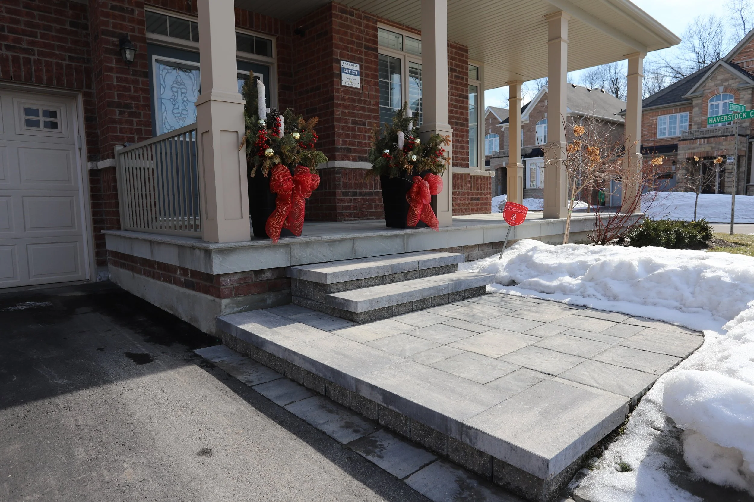 Front porch of a brick house with stone steps and two decorative planters with red bows, surrounded by snow.