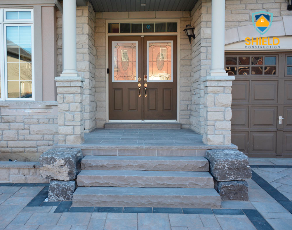 Front entrance of a house with double doors, stone steps, and pillars, adjacent to a garage.
