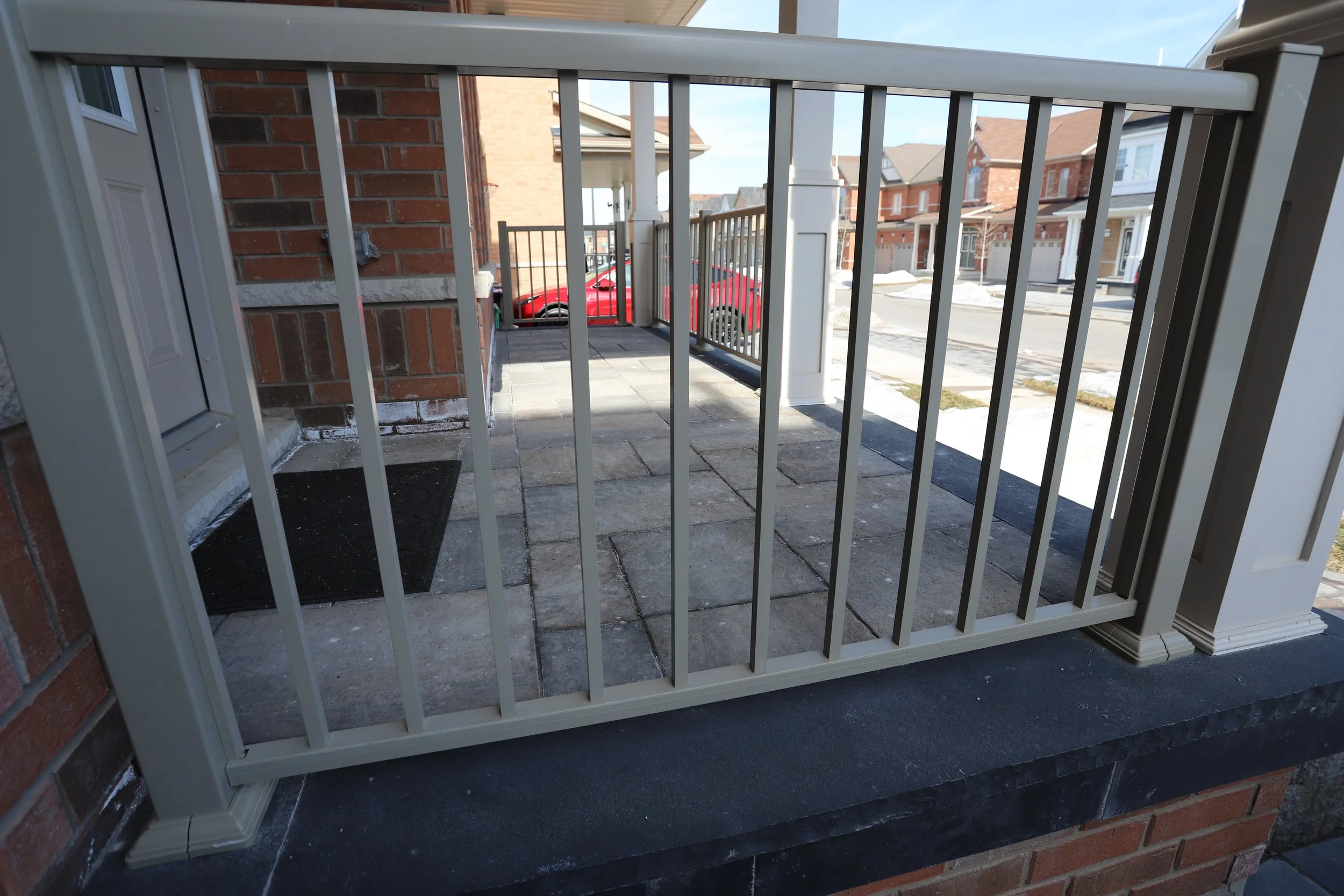 Front porch with metal railing and stone tiles, adjacent to a brick house, overlooking a suburban street.