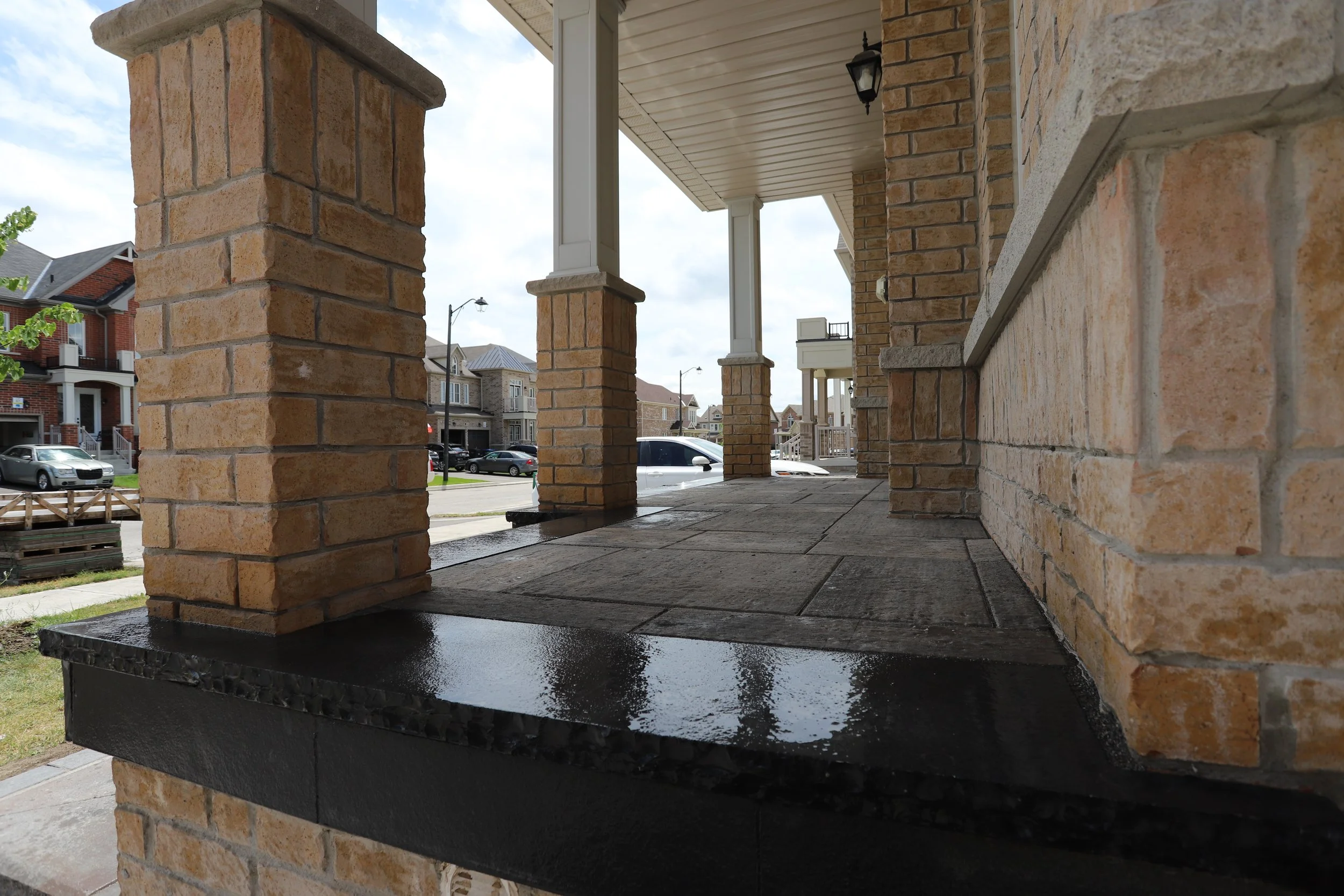 Brick porch with pillars, wet pavement, suburban neighborhood in background.