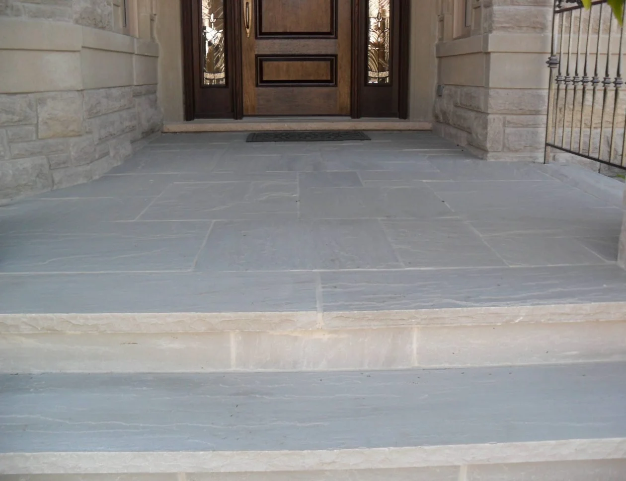 Stone porch and steps in front of a wooden door with decorative panels on a building facade.
