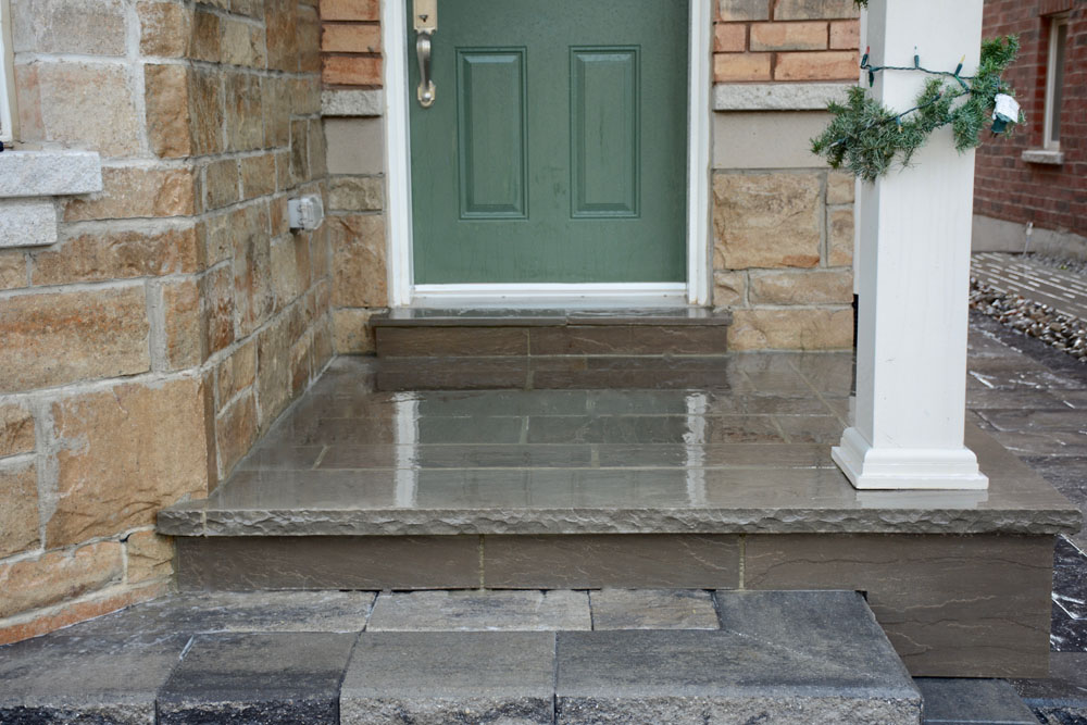 Front porch with stone steps, green door, and brick walls; holiday garland decor