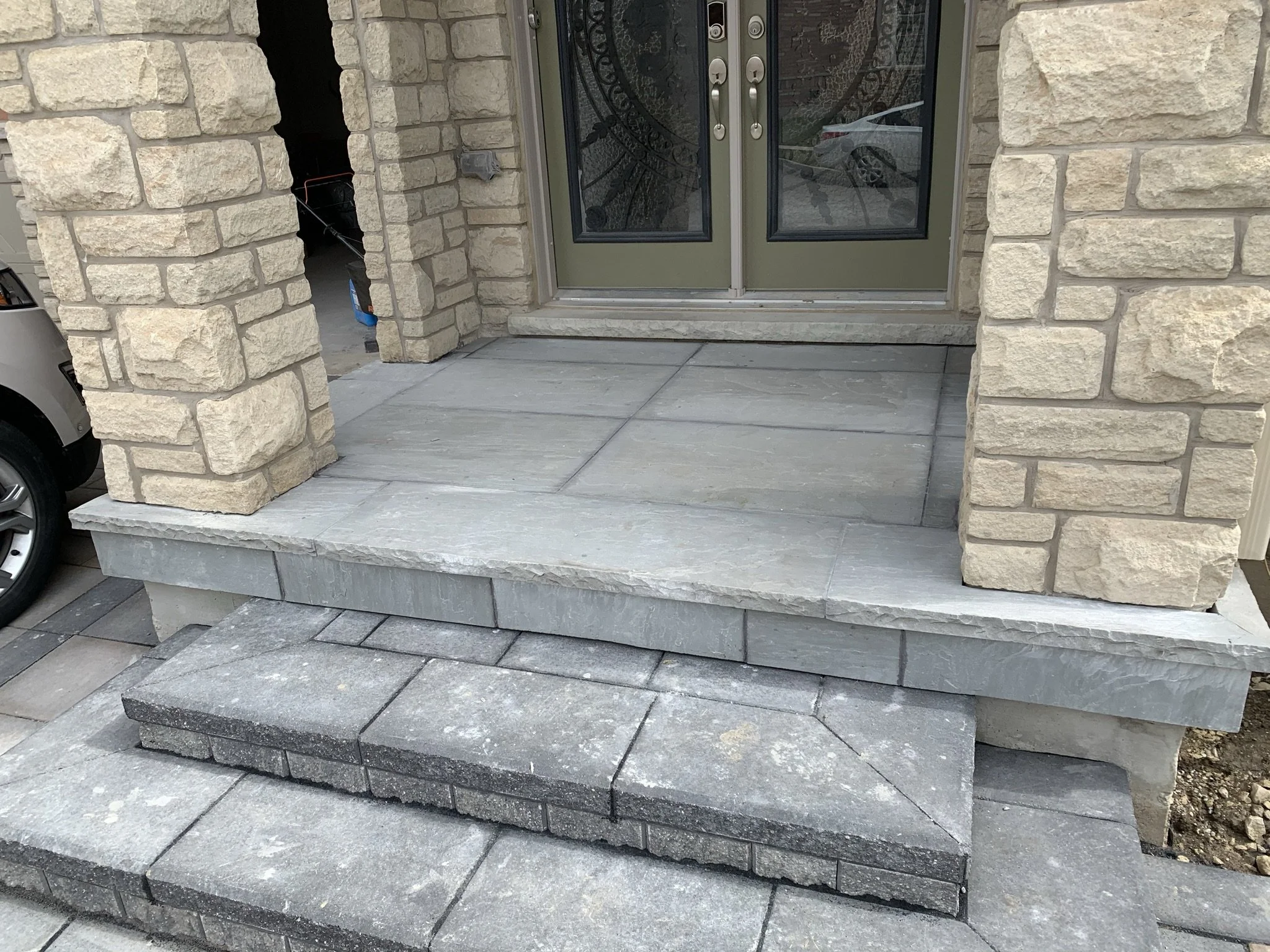 Front porch with stone pillars and gray tiled steps leading to double doors.