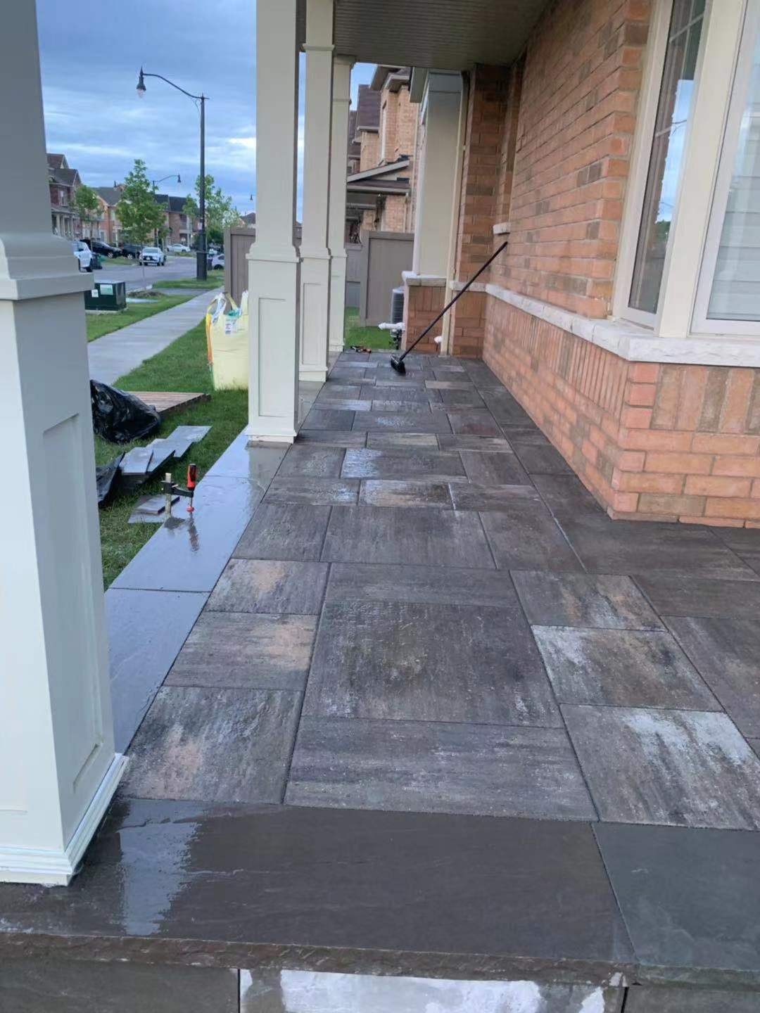 Front porch with wet paving stones, a brick house exterior, and a broom leaning against the wall.