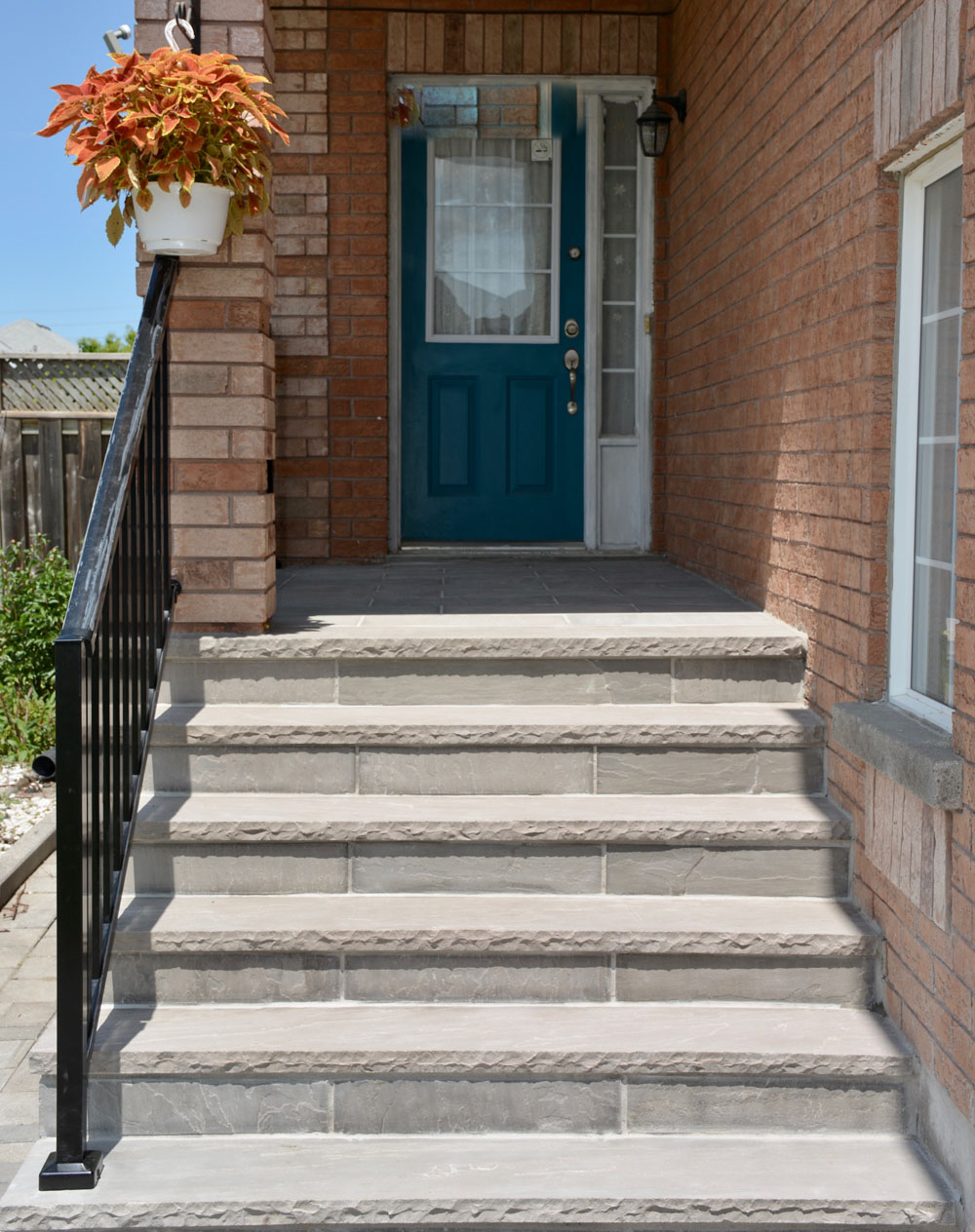Front steps leading to a blue entrance door with a potted plant on brick wall.