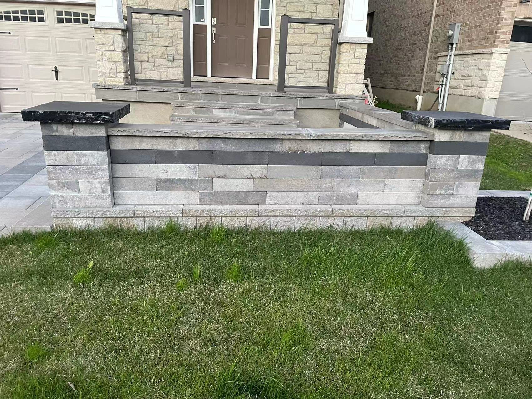 Stone porch wall with steps leading to a front entrance, surrounded by green grass and a garage visible in the background.