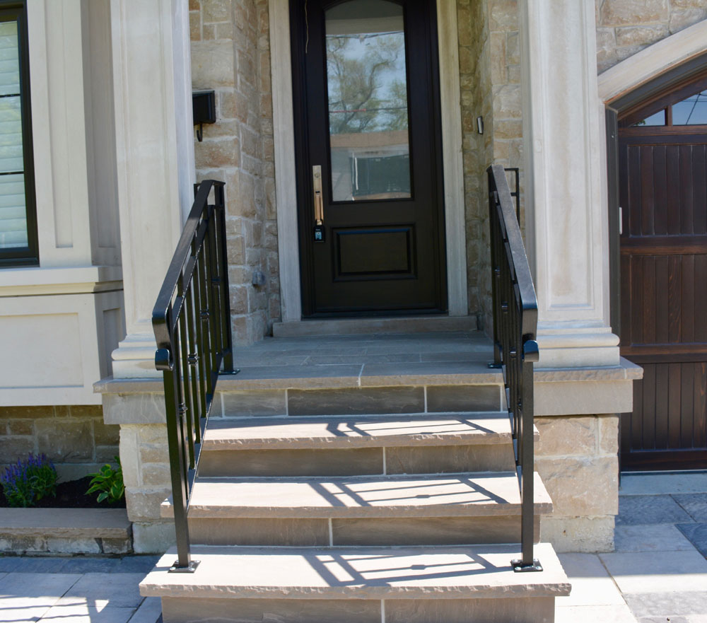 Entrance of a stone house with steps and black metal railings