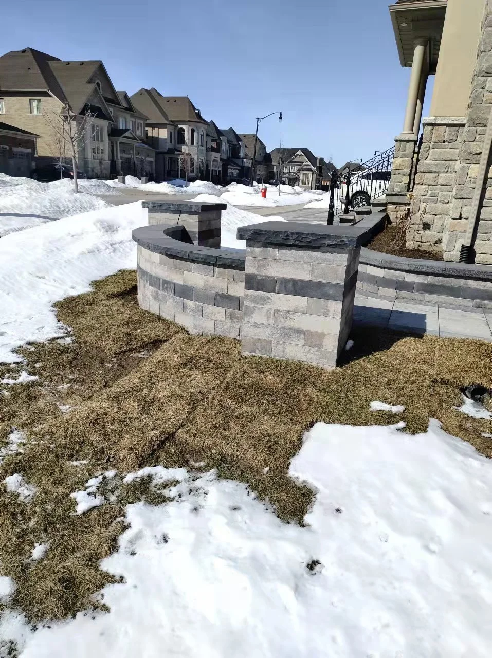 Snow-covered neighborhood with a stone wall and houses in the background.