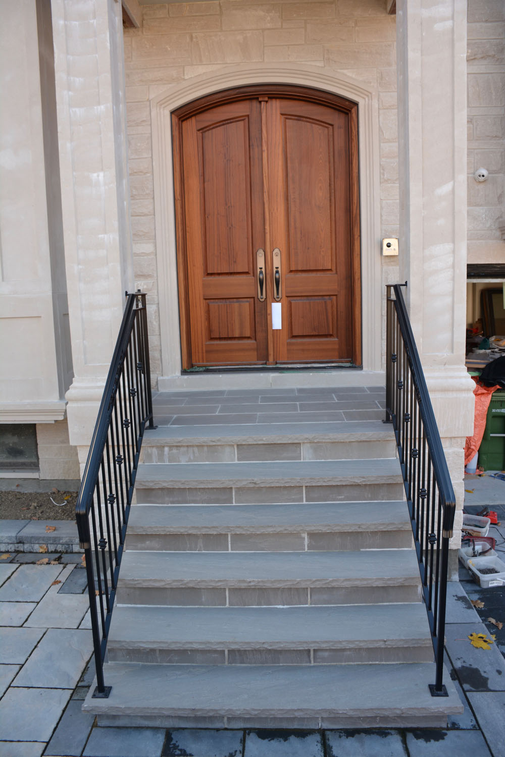 Stone steps leading to a wooden double front door flanked by black metal railings.