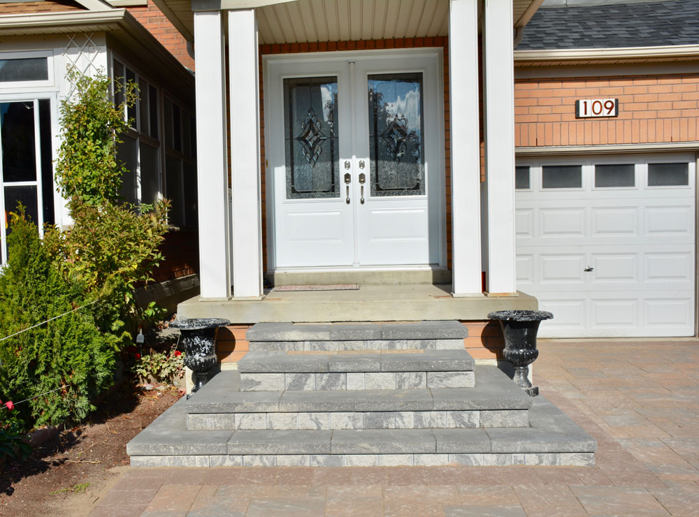 Front entrance of a house with a white door, decorative glass panels, and stone steps. Two dark-colored planters flank the entryway. The number 109 is displayed near a garage door to the right.