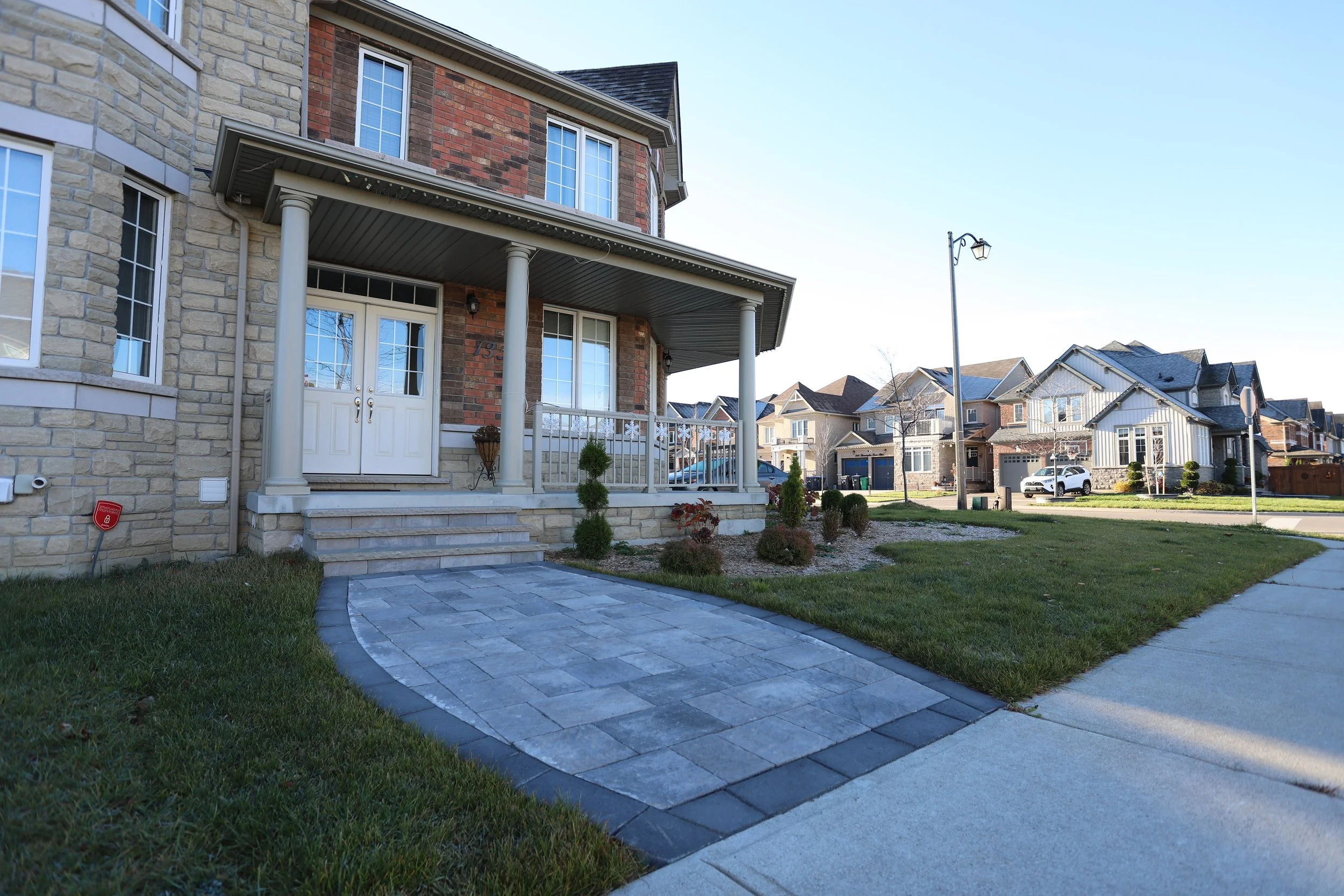 Exterior of a suburban two-story house with brick and stone facade, a covered porch, landscaped front yard, and a paved walkway.
