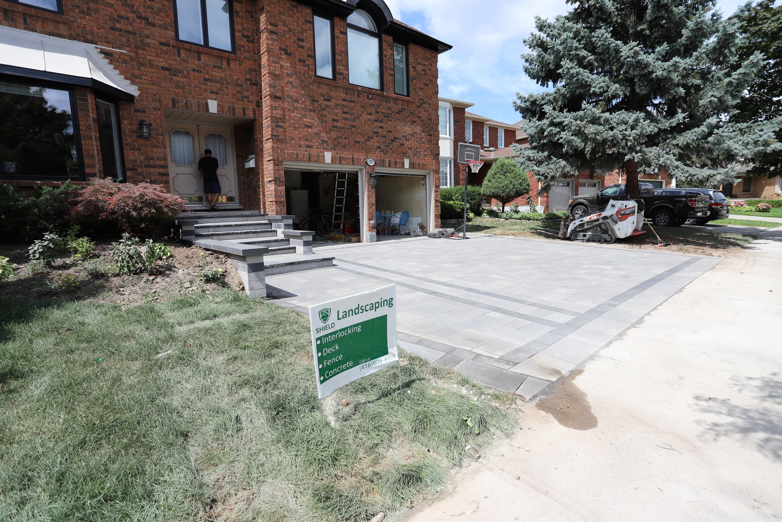 Brick house with new stone driveway, landscaping sign, and construction equipment.