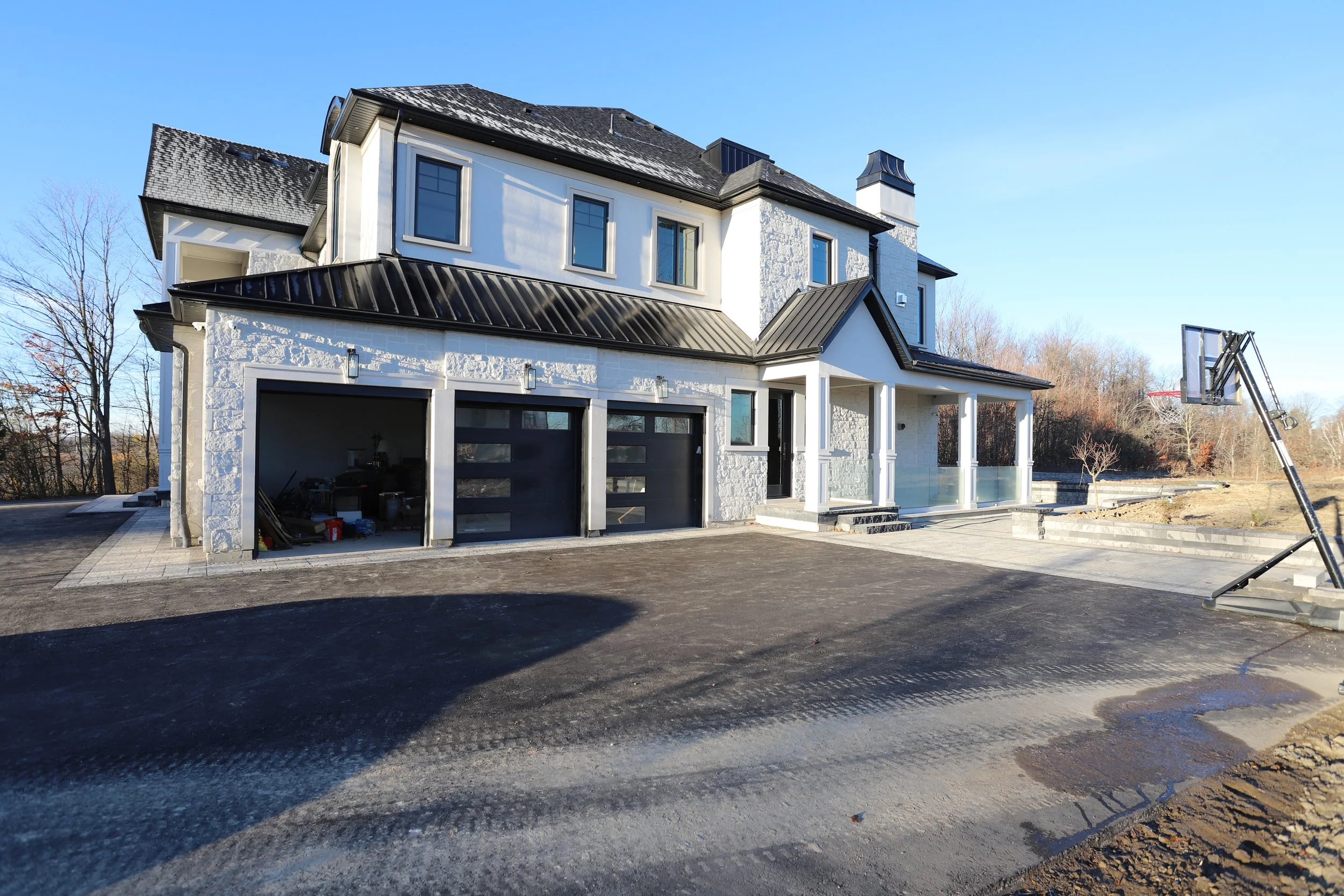 Modern two-story house with a black roof, garage, and basketball hoop in the driveway.