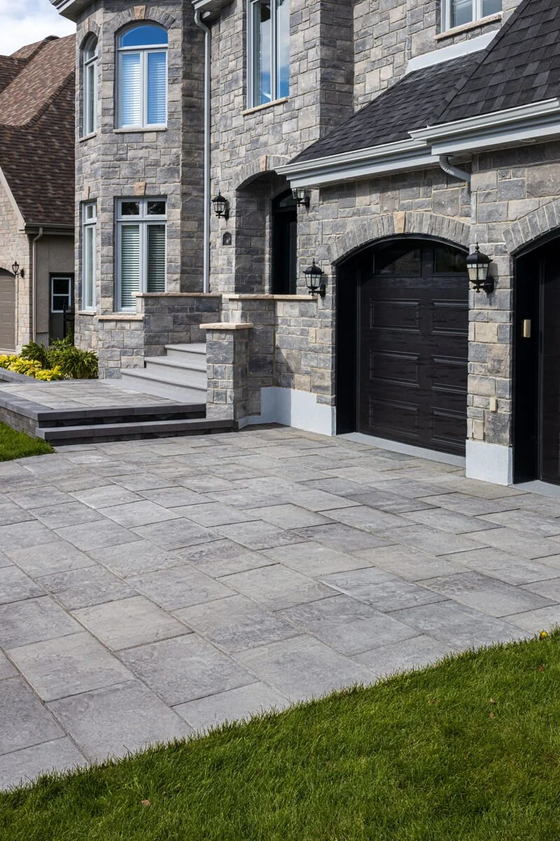 Residential home with stone exterior, black garage doors, and paved driveway.