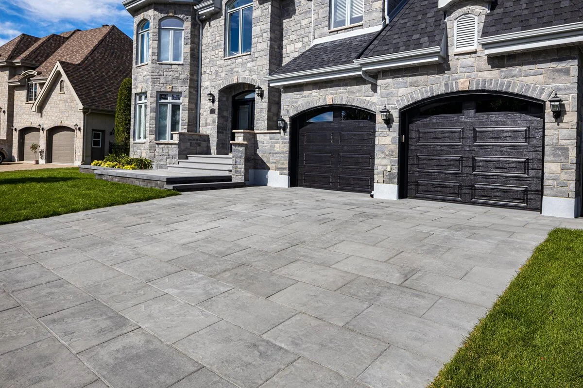 Stone driveway leading to a large brick house with dark garage doors