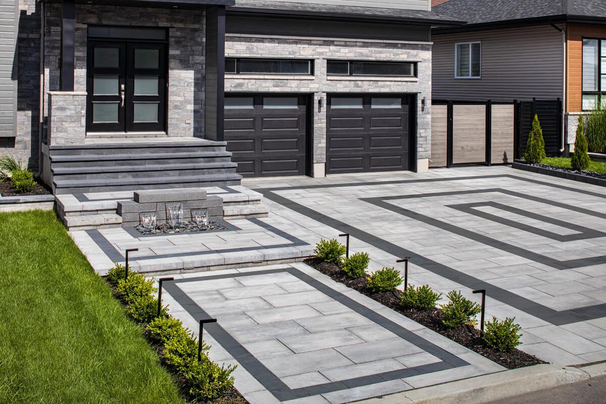 Modern house with symmetrical architecture, double black garage doors, gray stone front, integrated driveway and pathway pattern, and landscaped hedges.
