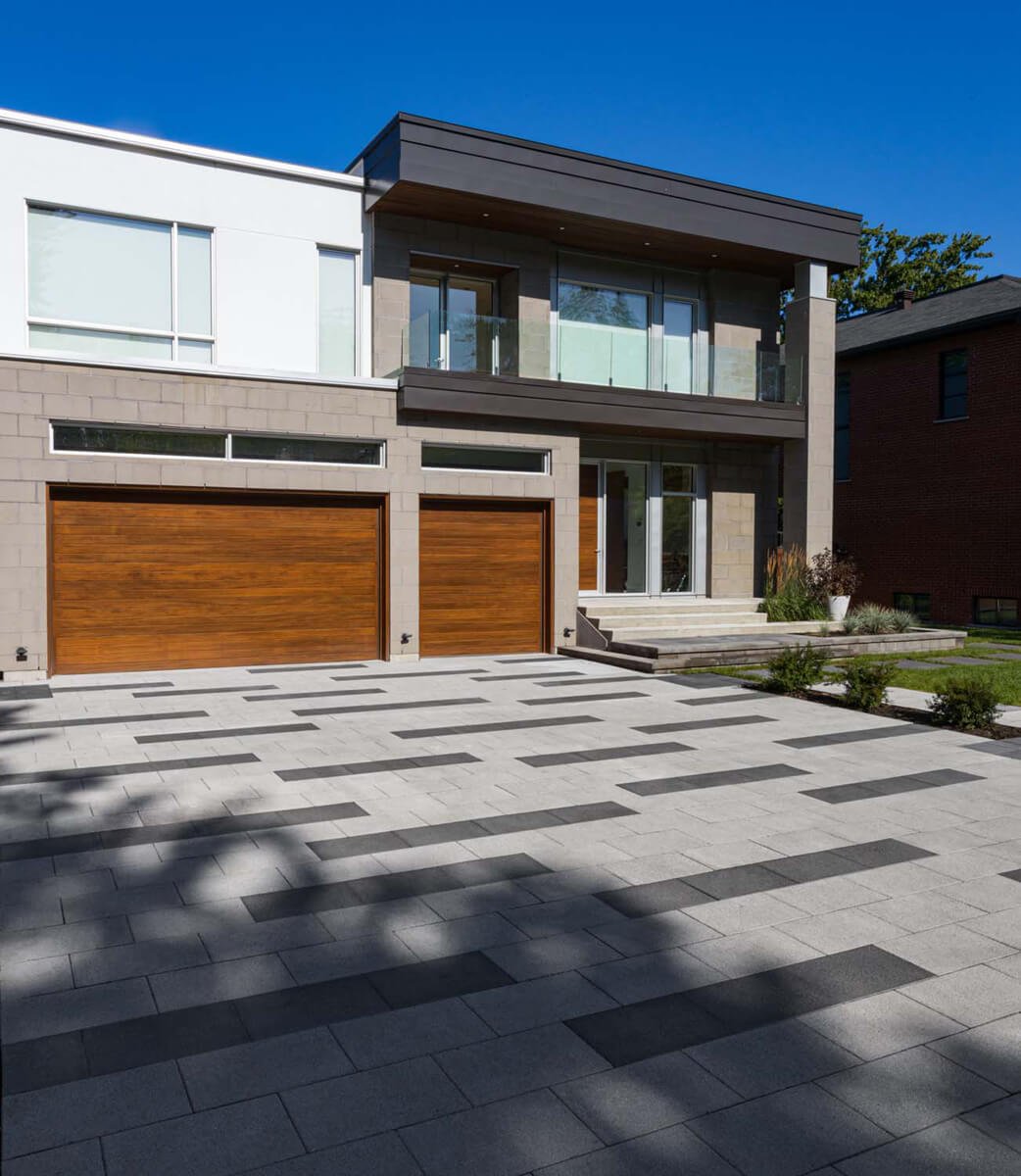 Modern two-story house with a large driveway and two wooden garage doors. The exterior features a mix of light and dark paneling.