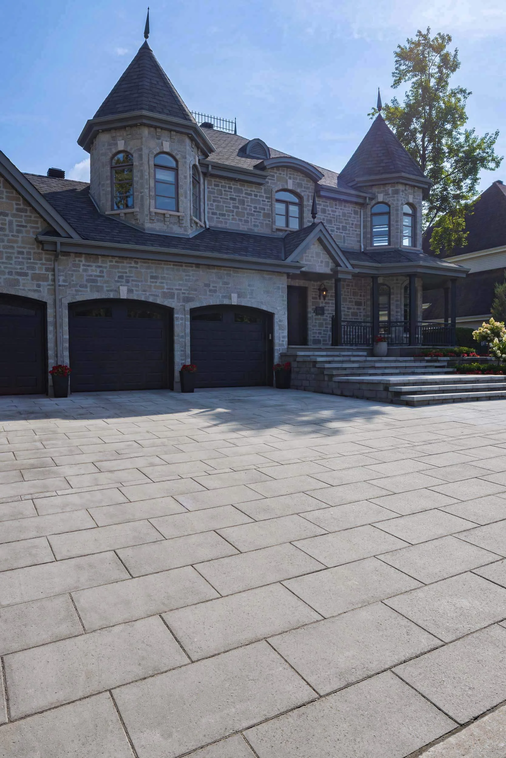 Luxury stone house with turrets, paved driveway, three-car garage, and landscaped garden.