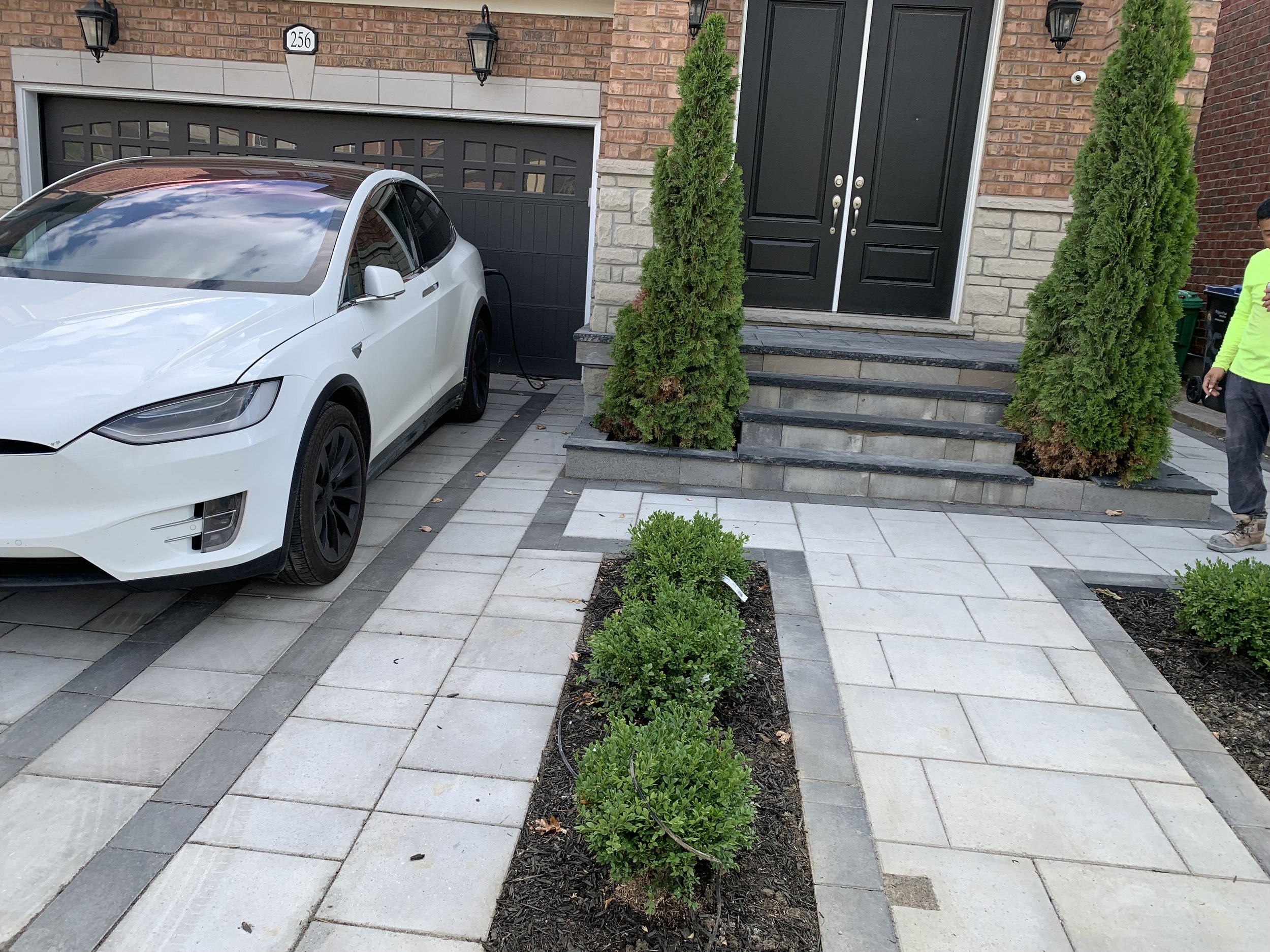 White electric car parked in driveway in front of a garage, with brick house entrance and landscaped walkway.