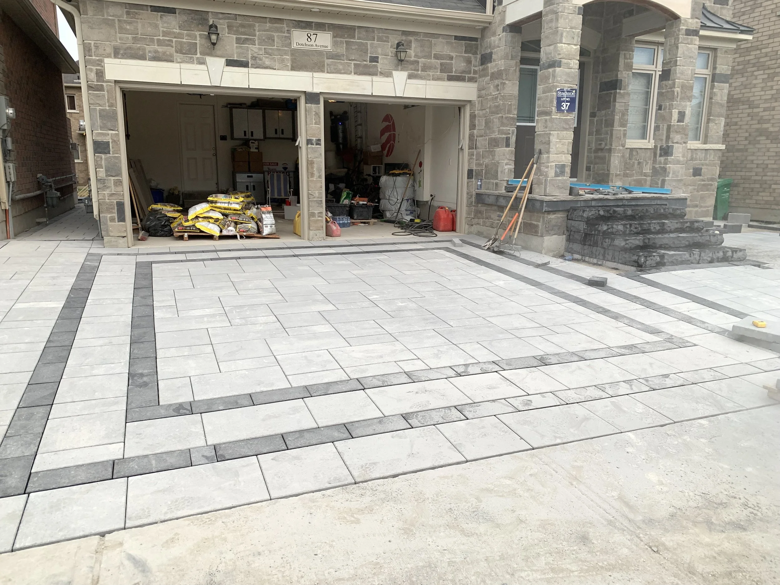 Newly paved driveway with stone tiles near a garage, featuring construction materials and tools.
