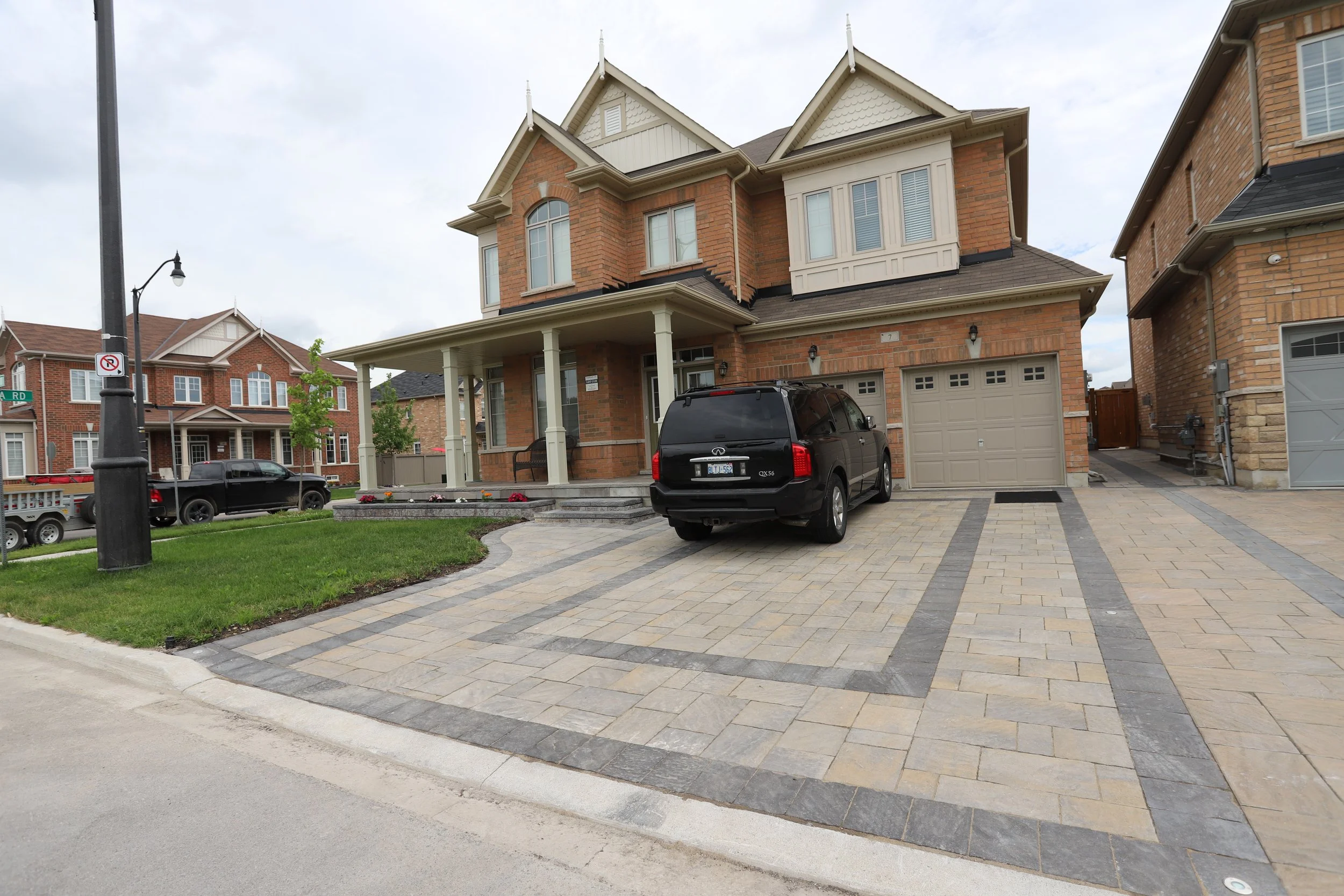 Suburban two-story brick house with a two-car garage, a black SUV parked on the driveway, and a landscaped front yard.