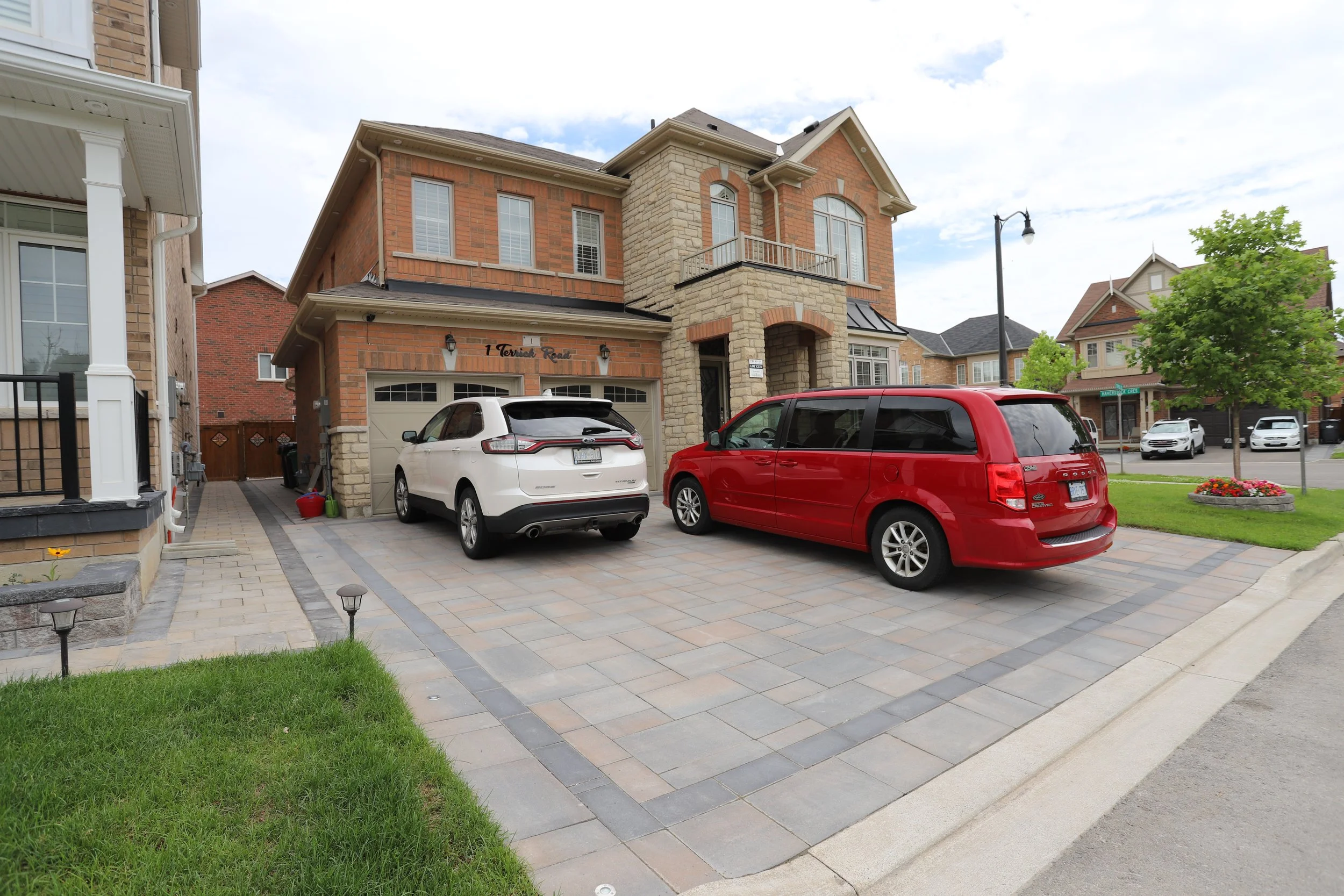 Suburban house with driveway and parked cars, including a white SUV and red minivan.