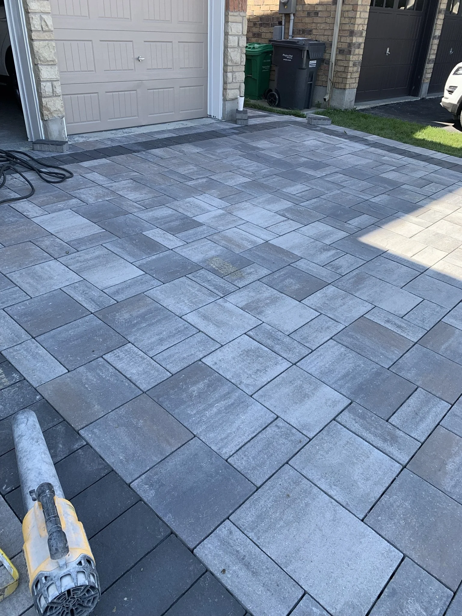 Newly installed driveway with interlocking stone pavers, adjacent garage door, and outdoor blower.