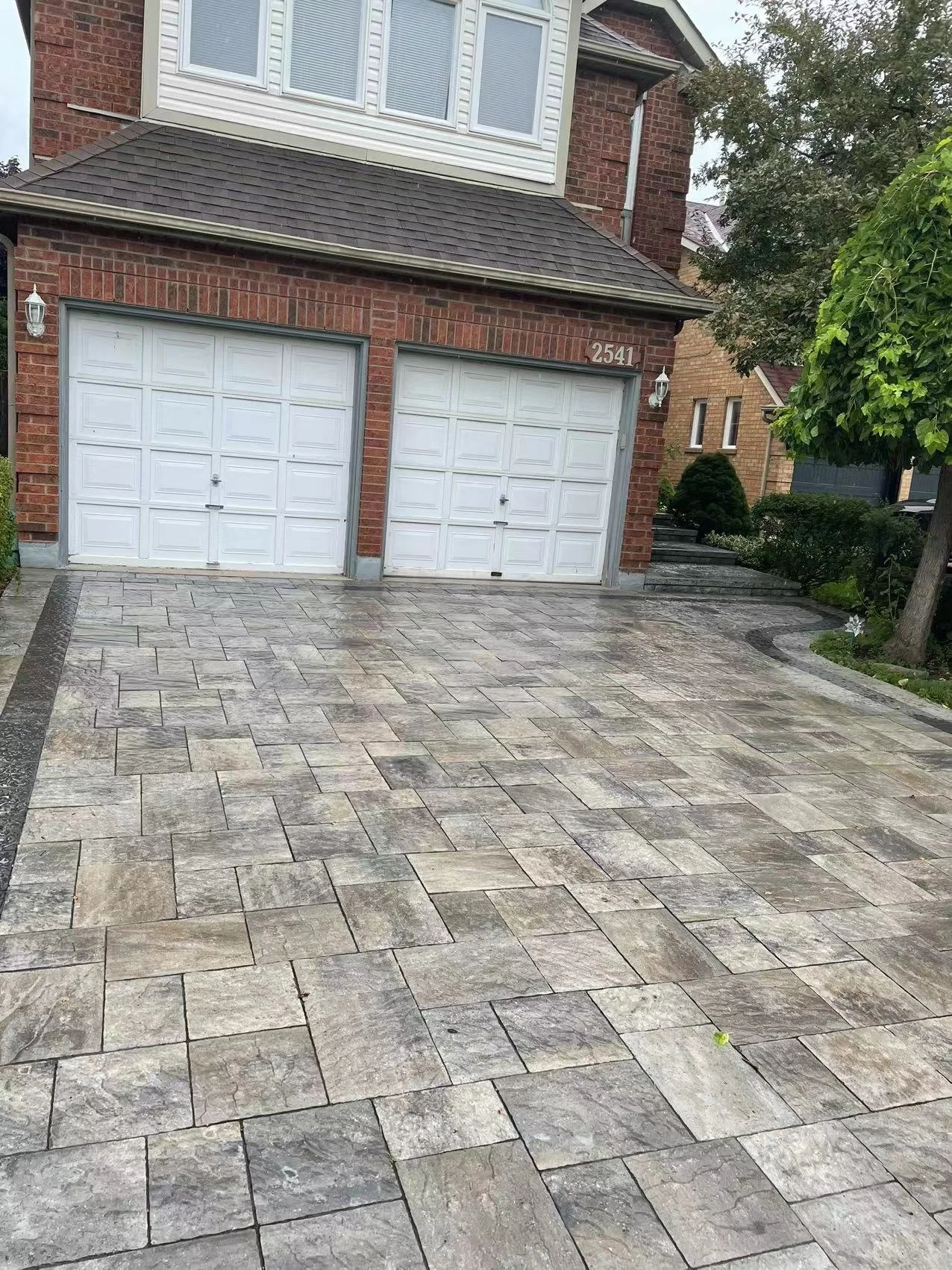 Driveway with stone pavers and a two-car garage on a brick house.