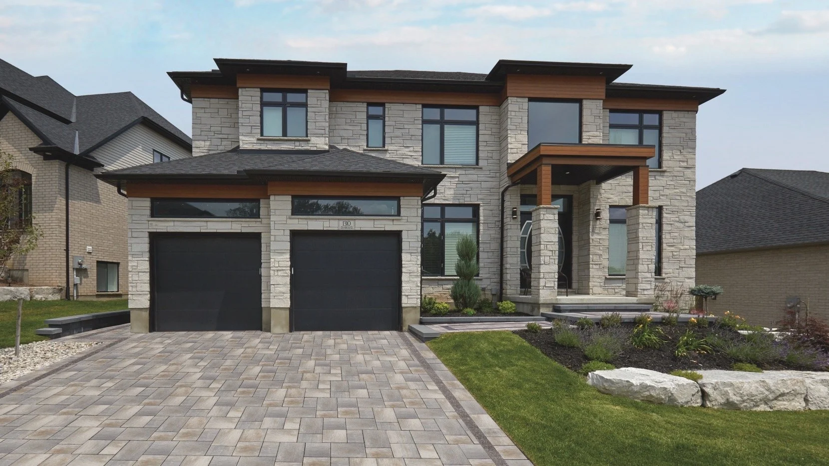 Modern two-story house with stone facade, black garage doors, and landscaped front yard.