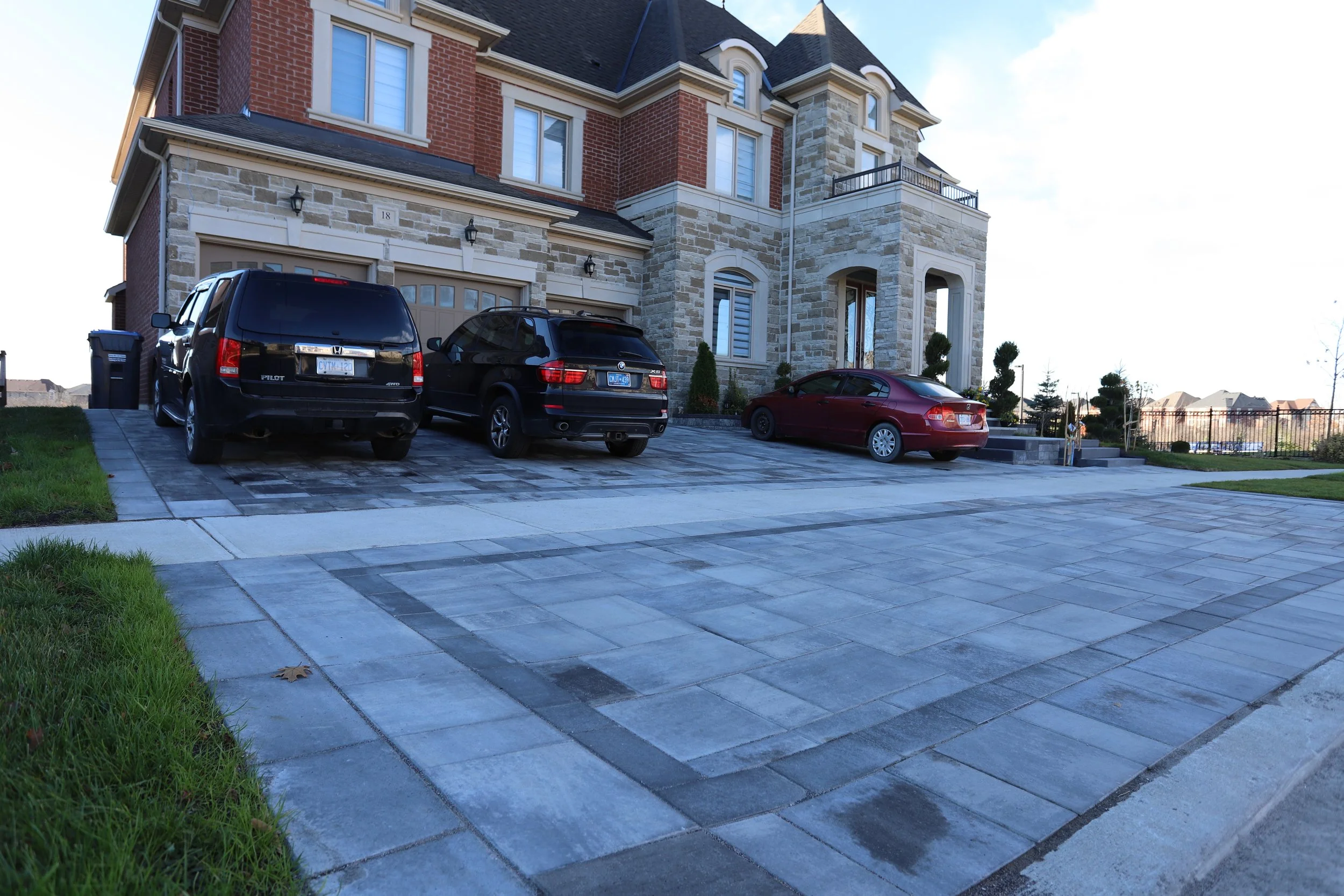 Driveway with three cars parked outside a large brick and stone house.
