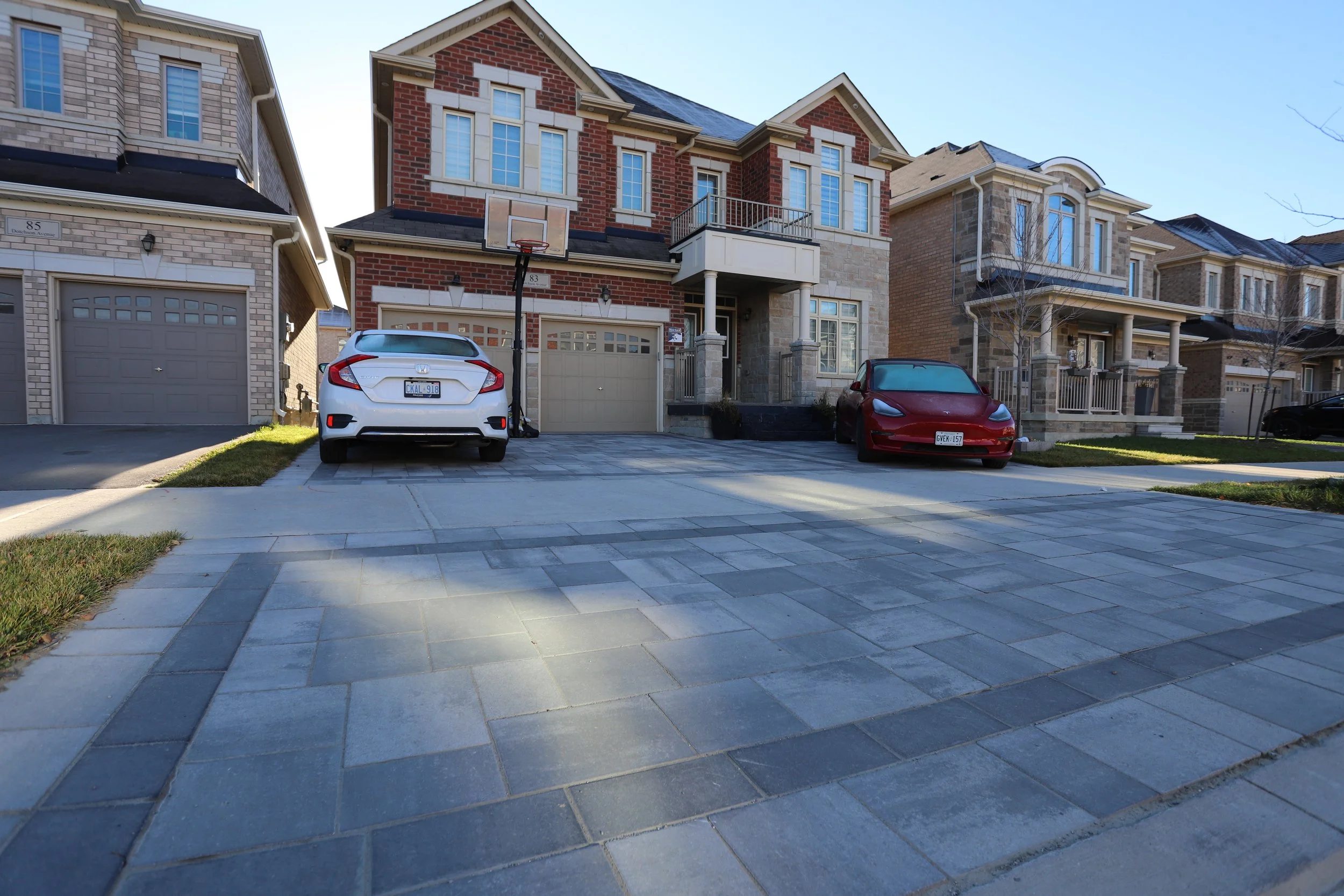 Suburban street with row of modern brick houses and two cars parked on driveways.
