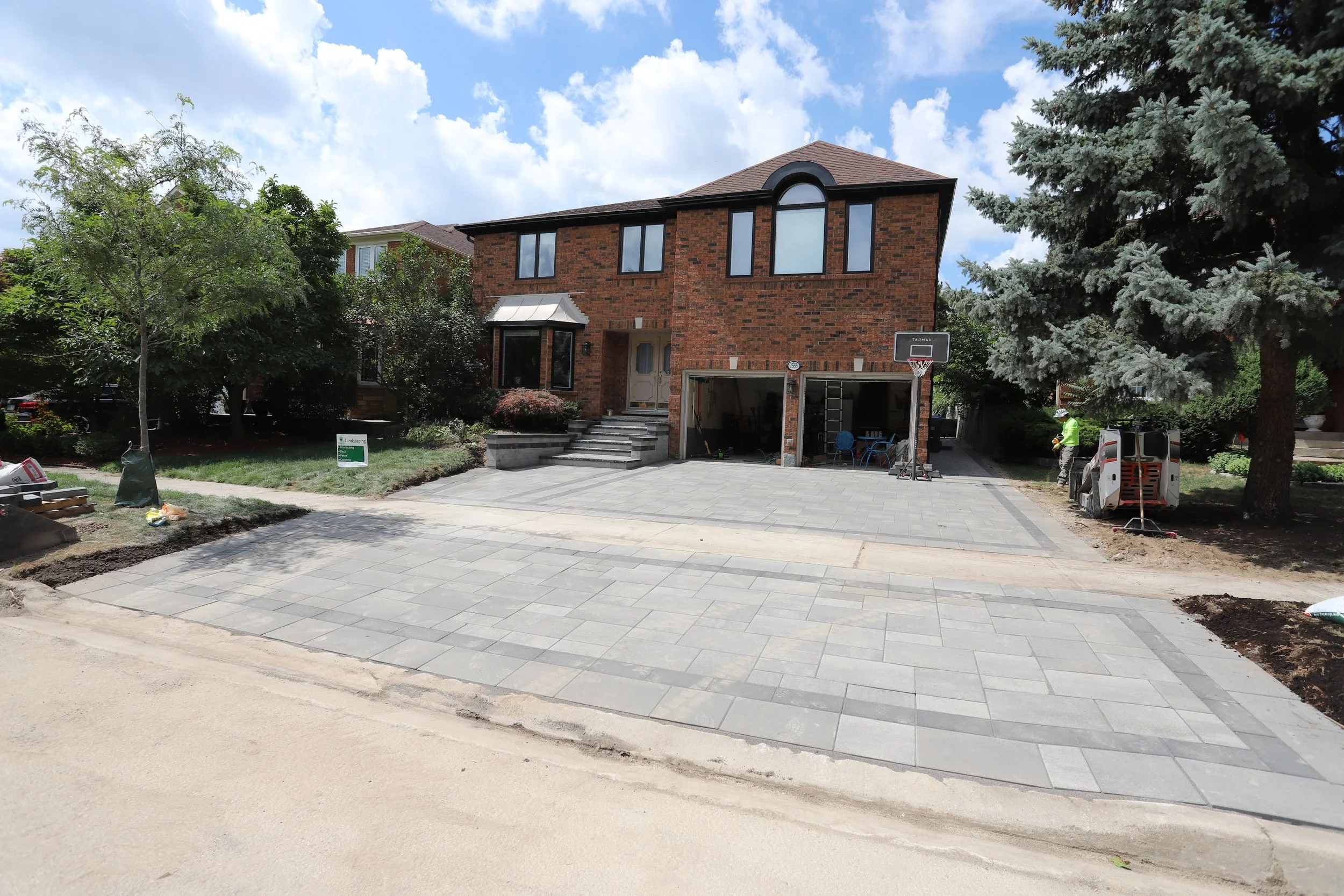 Brick house with new paved driveway, garage, and basketball hoop, surrounded by trees.