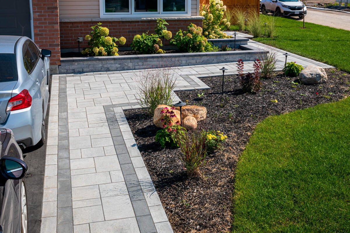 Modern landscaped front yard with a paved driveway, flower beds, and a parked silver car.