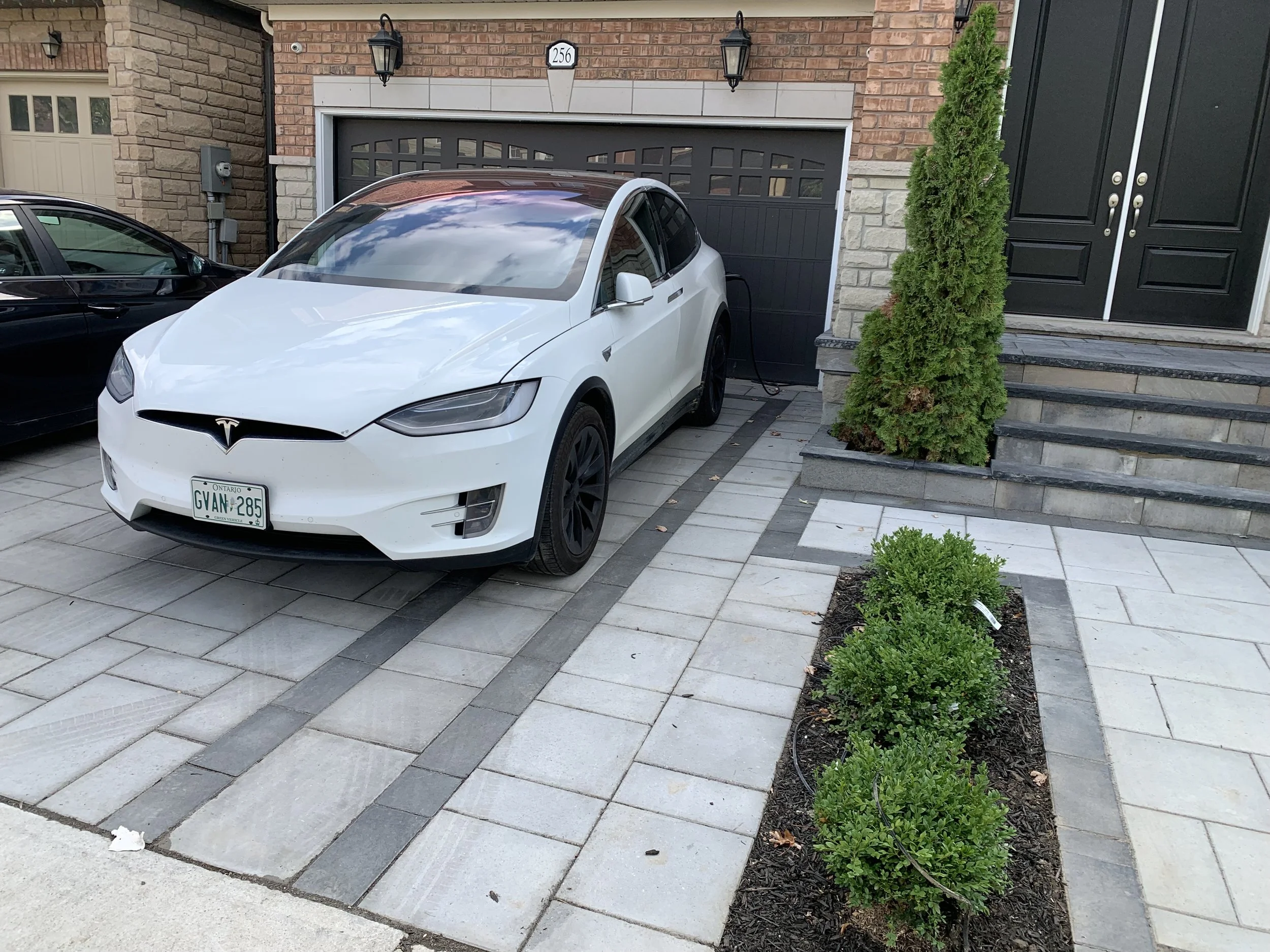 White Tesla Model X parked on a driveway with a landscaped pathway and shrubs.