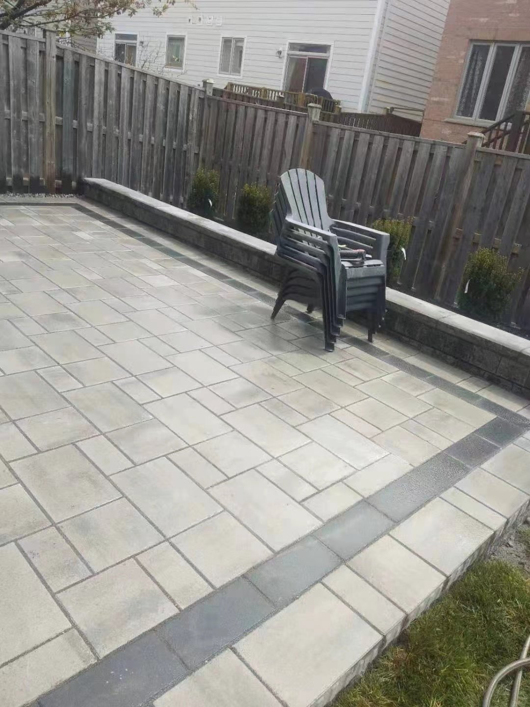 Outdoor patio with stacked black chairs, surrounded by a wooden fence and neighboring buildings.