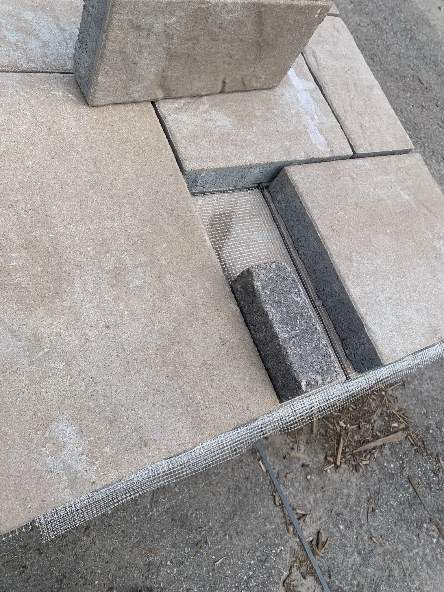 Close-up of arranged concrete paving stones with mesh underneath on a dirt surface.