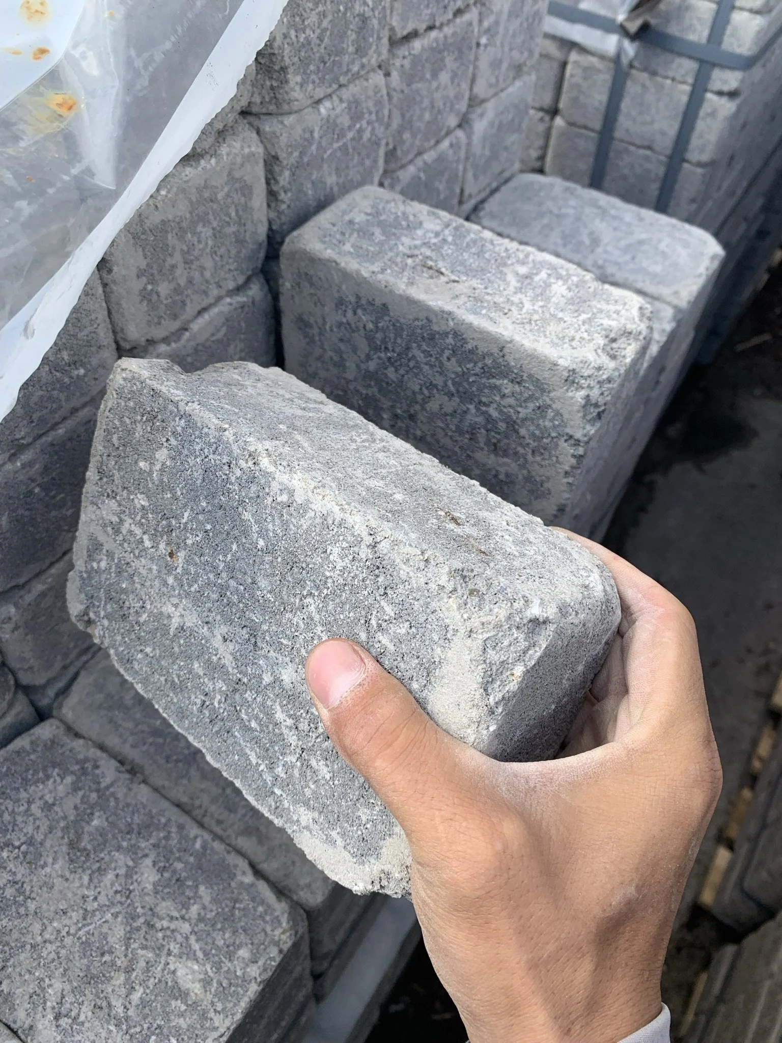 Person holding a gray rectangular paving stone among stacked pavers.