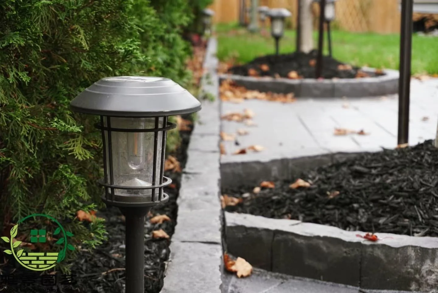 Outdoor garden pathway with decorative landscape lighting, mulch, and stone border, surrounded by green shrubs and grass.