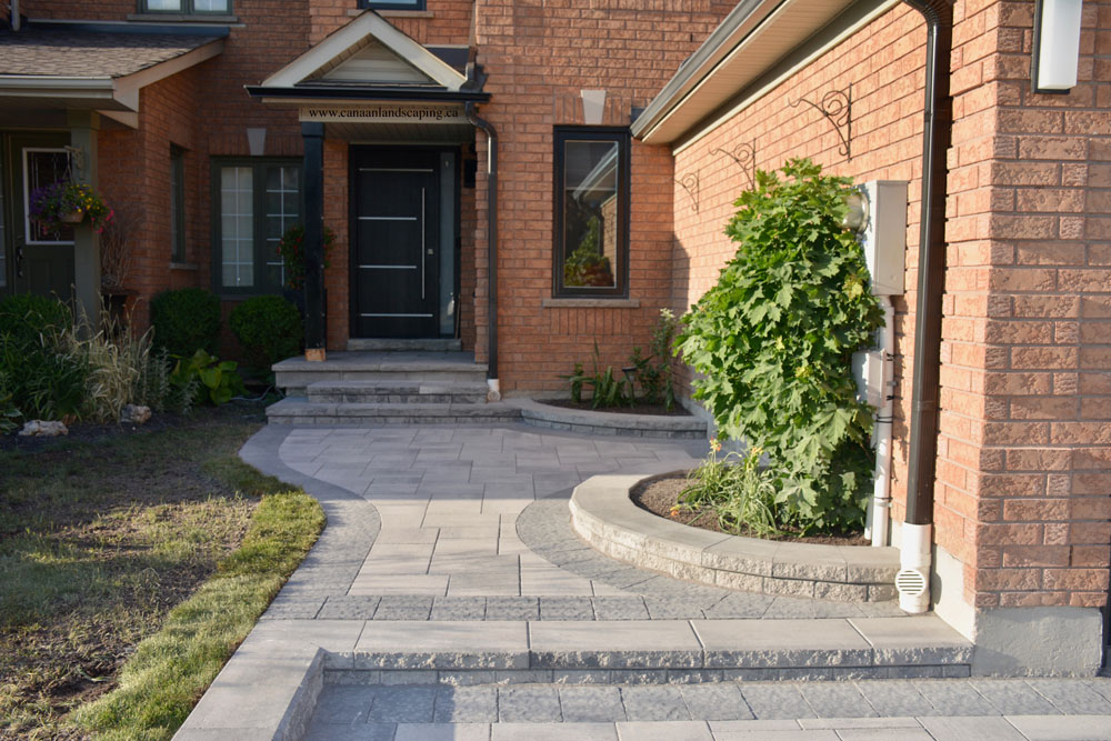 Front entrance of a brick house with a paved walkway, steps, and landscaping