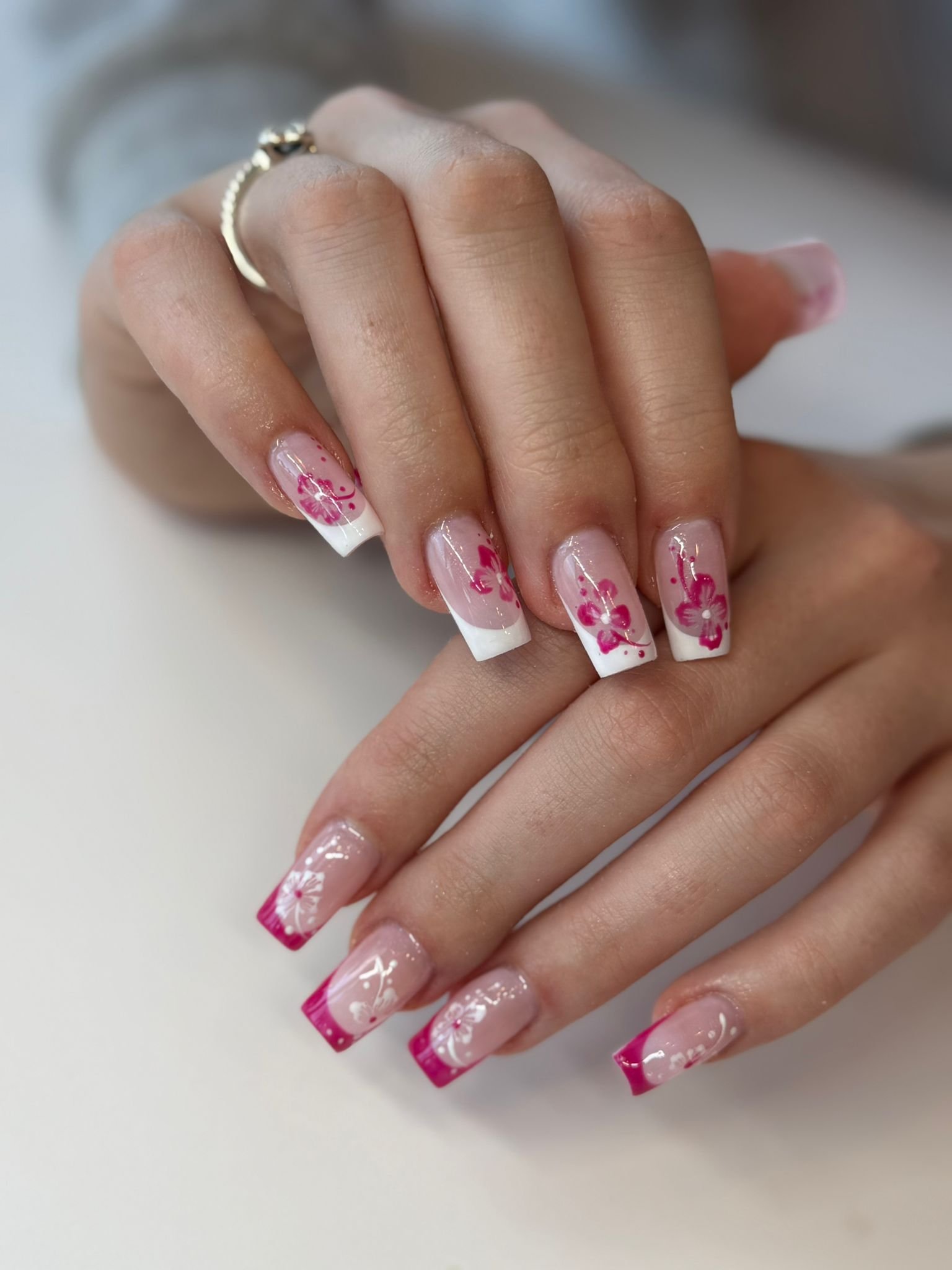 Close-up of hands with manicured nails featuring pink flower nail art, French tips, and pink tips.